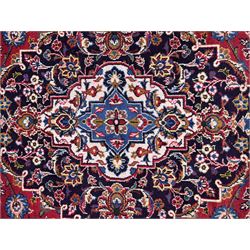 Large Kashan crimson ground carpet, central indigo medallion with stylised floral motifs, flanked by matching spandrels, bordered by multiple bands featuring repeating foliate and floral designs throughout