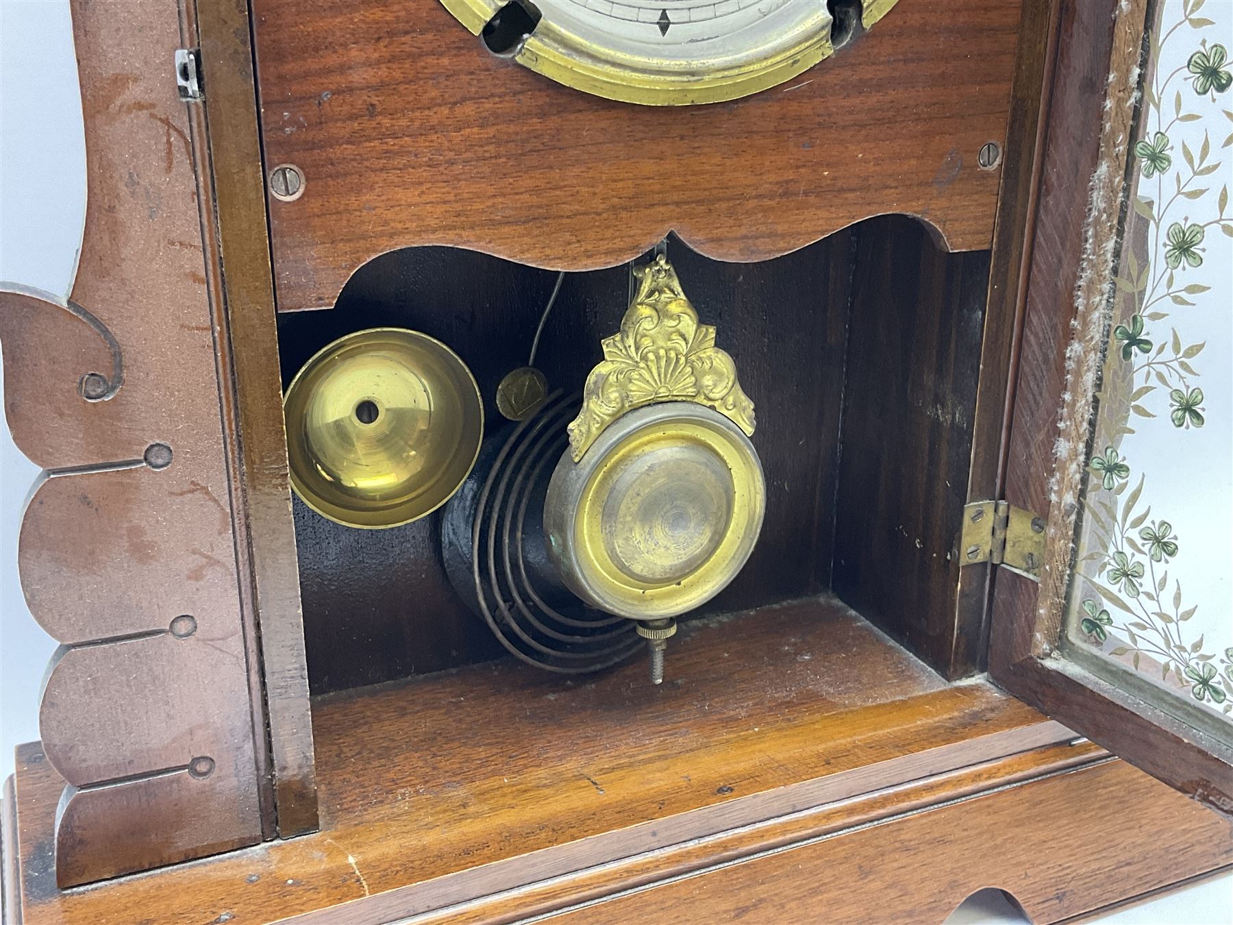 An early 20th century spring driven alarm clock in the style of an American  “gingerbread” shelf clock, rectangular wooden case with applied incised mouldings on a shaped taper foot plinth, full length glazed door with flowers and leaves, visible gilt pendulum bob, with a painted white metal dial inscribed “Fattorini & Sons Patent Automatic Alarm”, roman numerals and minute track with brass alarm setting disc, steel spade hands, spun brass bezel with winding apertures, alarm sounding on both a coiled gong and bell, two advertising/trade labels pasted to the case backboard.