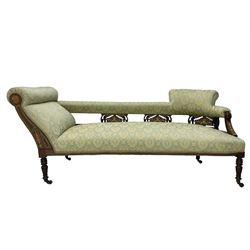 Late Victorian walnut salon settee or chaise lounge, double-ended with rolled back and curved end, upholstered in light aquamarine fabric with raised repeating lozenge pattern, decorated with laurel leaf wreaths and urns, three pierced splats carved with curled leaves, inlaid with dolphins and scrolled foliate motifs in simulated ivory and boxwood, on tapering ring turned supports with brass and ceramic castors (L166, D60, H70cm); together with matching tub-shaped armchair (W61cm, H73cm, D66cm)  