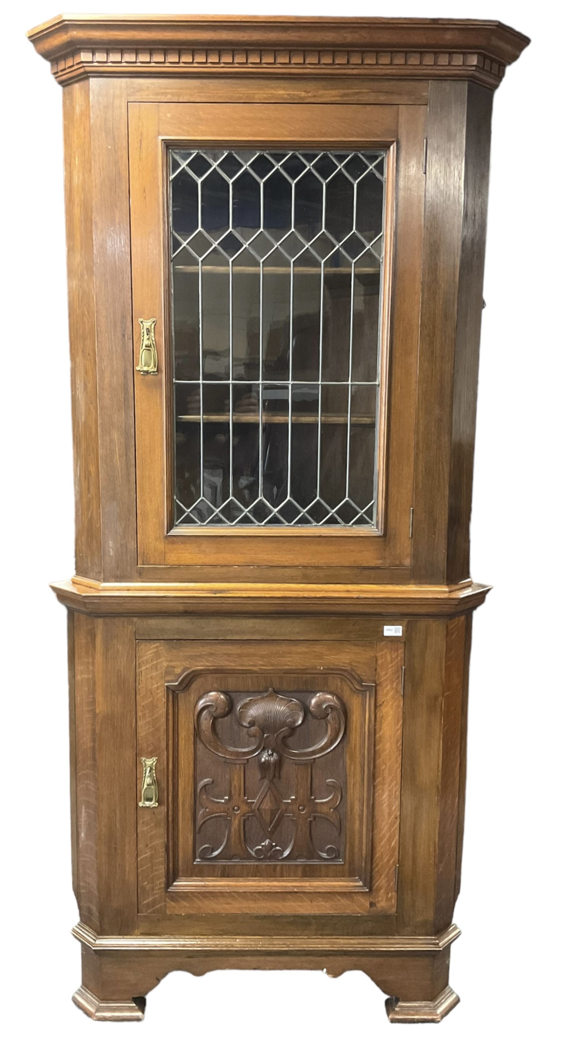 Arts & Crafts period oak corner cabinet, projecting cornice over astragal glazed door and single panelled door decorated with applied carved foliate scrolls and stylised roods surrounded by moulded edge, enclosing single shelf