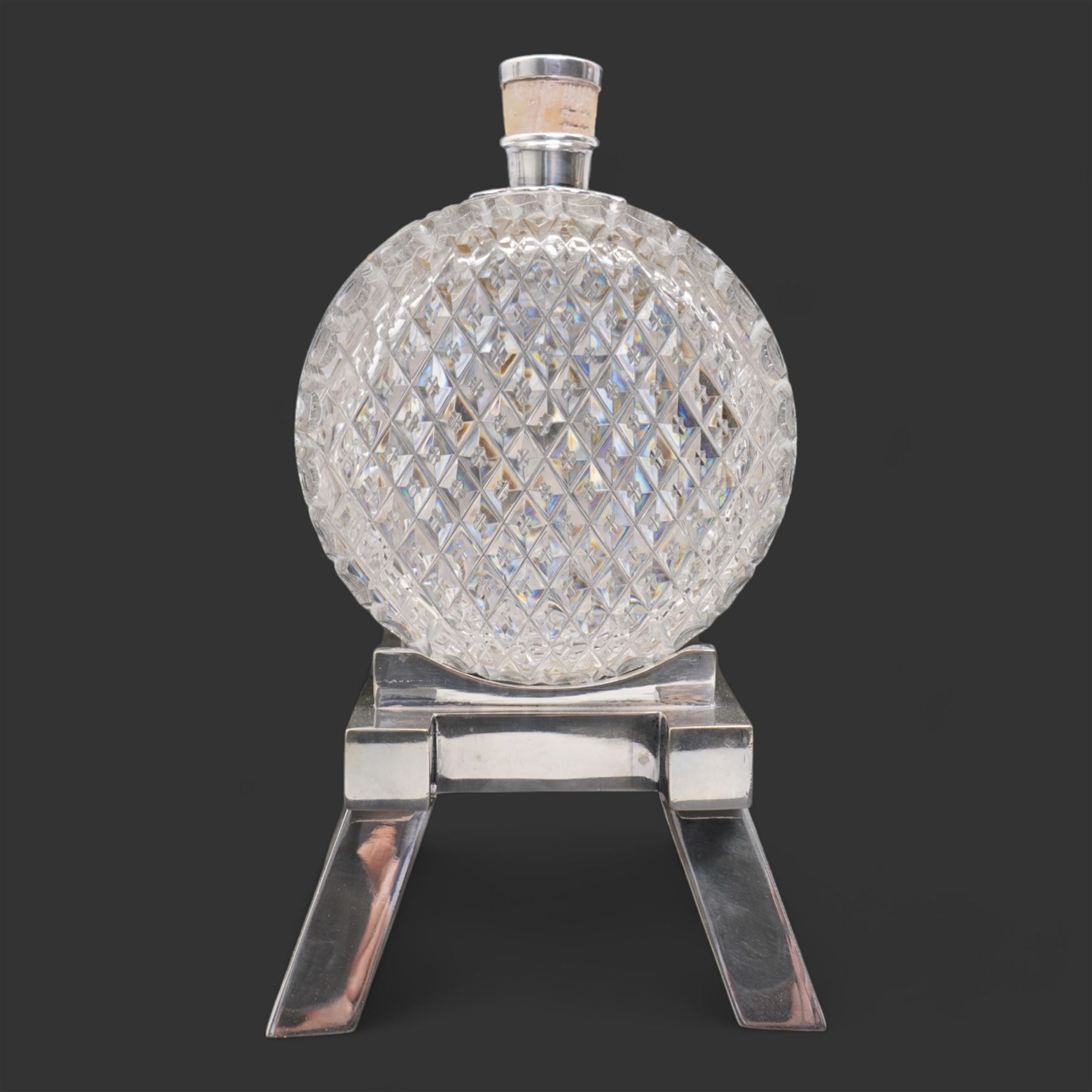 Late 19th/ early 20th century cut glass and silver plate whisky decanter by John Grinsell & Sons, of barrel form, with cork stopper and silver plate strapwork mounts, the tap suspending a bucket form measure, on trestle form support, H24cm x L24cm 