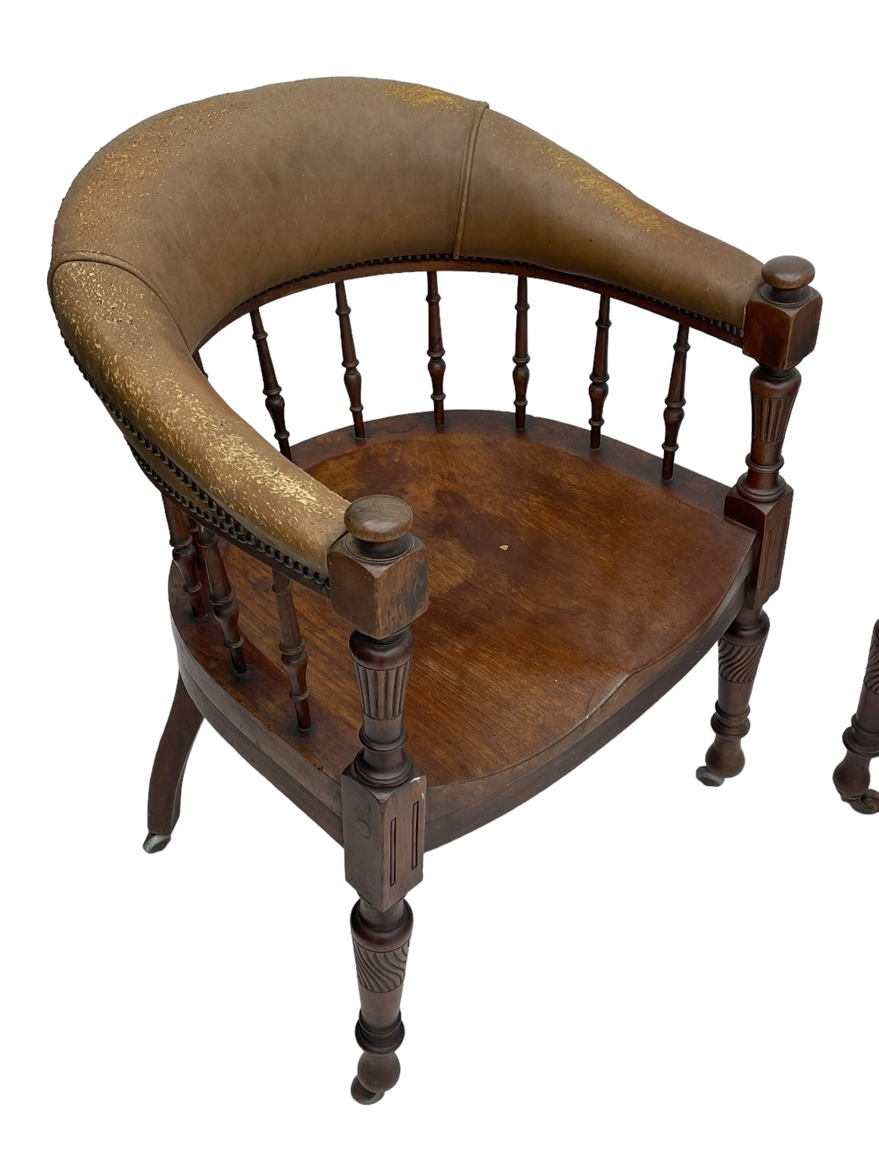 Pair of late Victorian walnut tub-shaped elbow chairs, the cushioned cresting rail upholstered in leather on spindle turned supports, dished saddle seat on turned supports