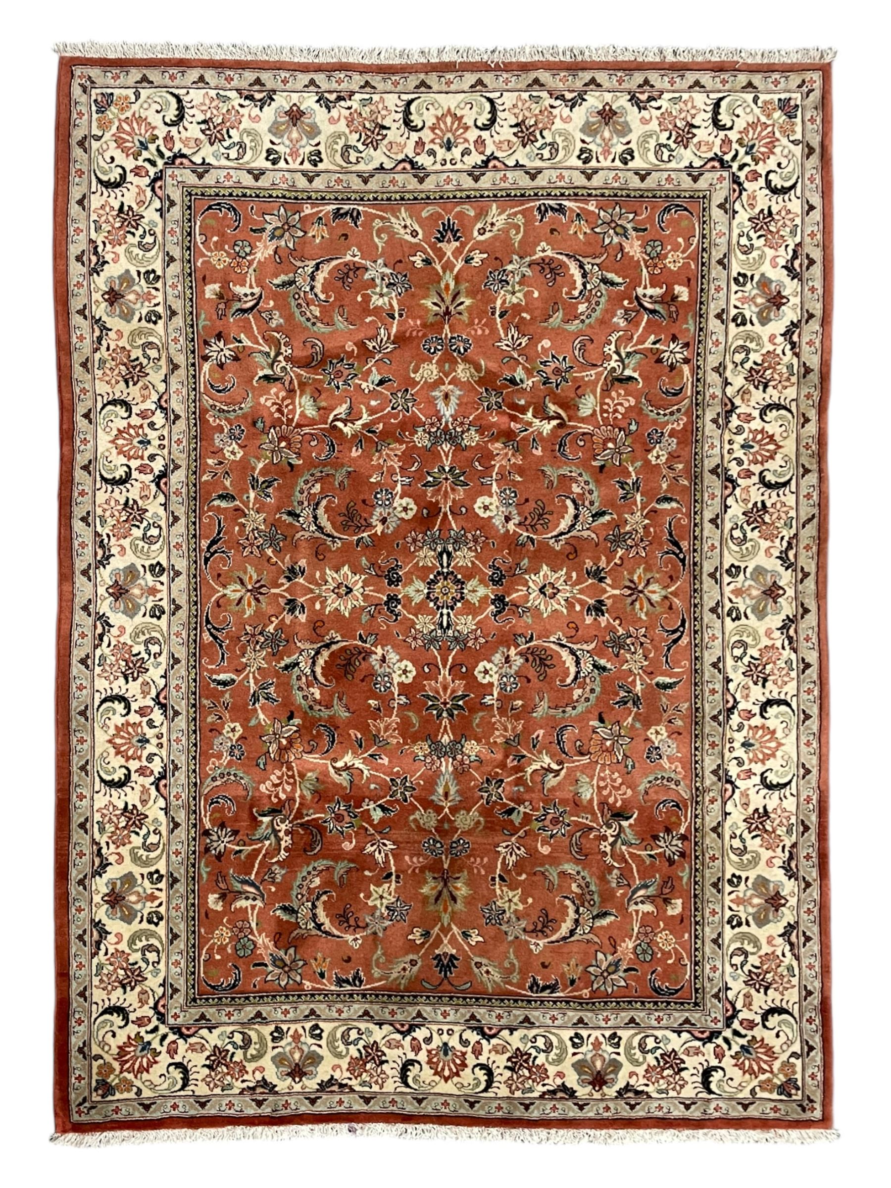 Persian Kashan peach ground rug, the field decorated with swirling leafy branches and stylised plant motifs, ivory ground border with trailing foliate design interspersed with flower heads, within guard stripes 