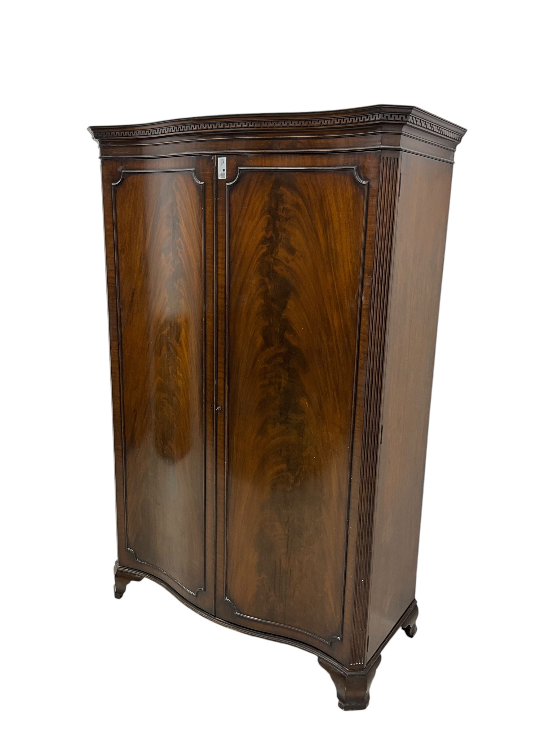 Early 20th century mahogany serpentine double wardrobe, moulded cornice over two figured doors, the interior fitted with hanging rail and shelf, canted and fluted uprights, on bracket feet 