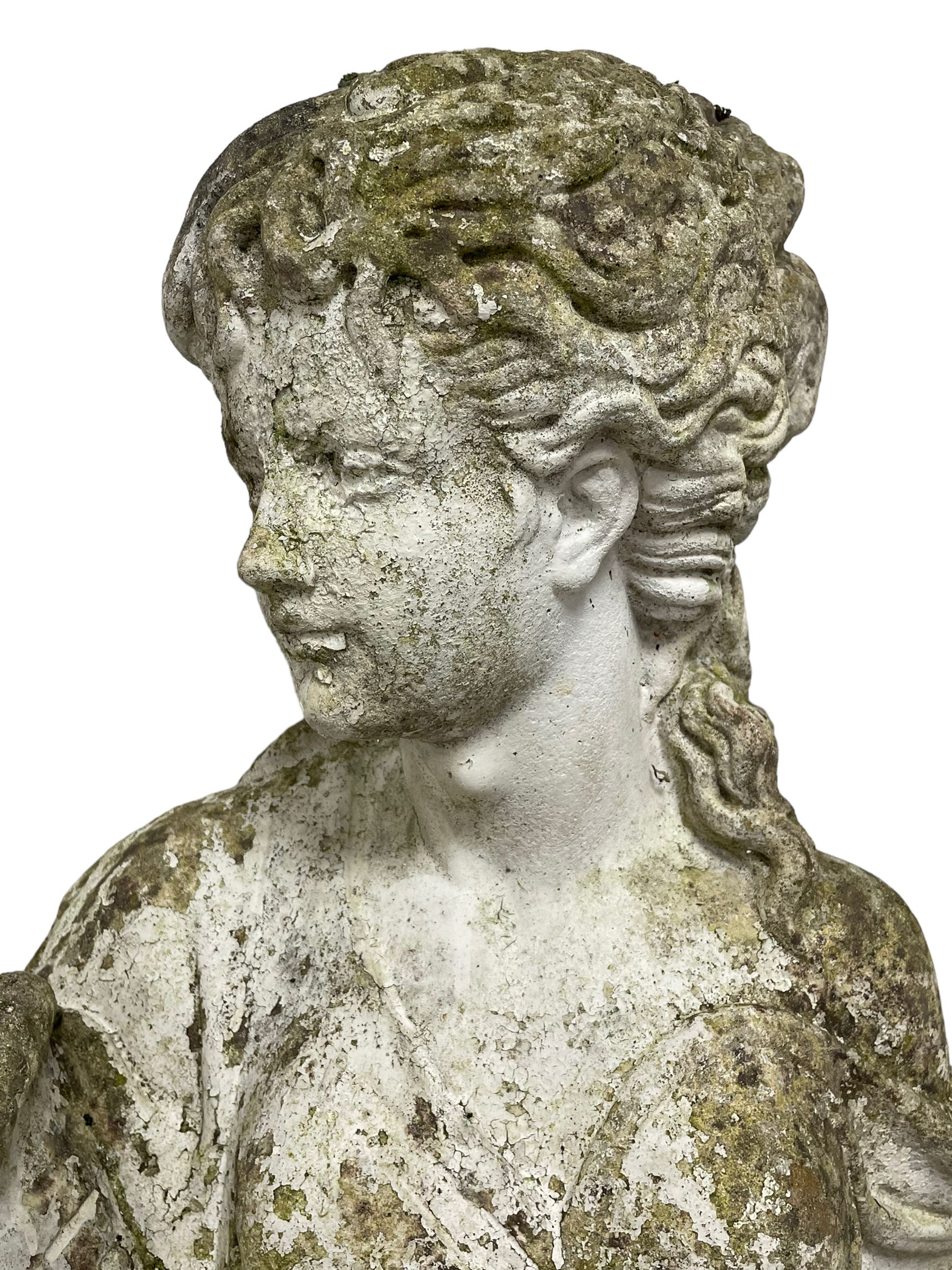 Weathered and painted cast stone garden statue, in the form of an Italian maiden carrying baskets with gathered flora and berries, on a shaped ovoid base