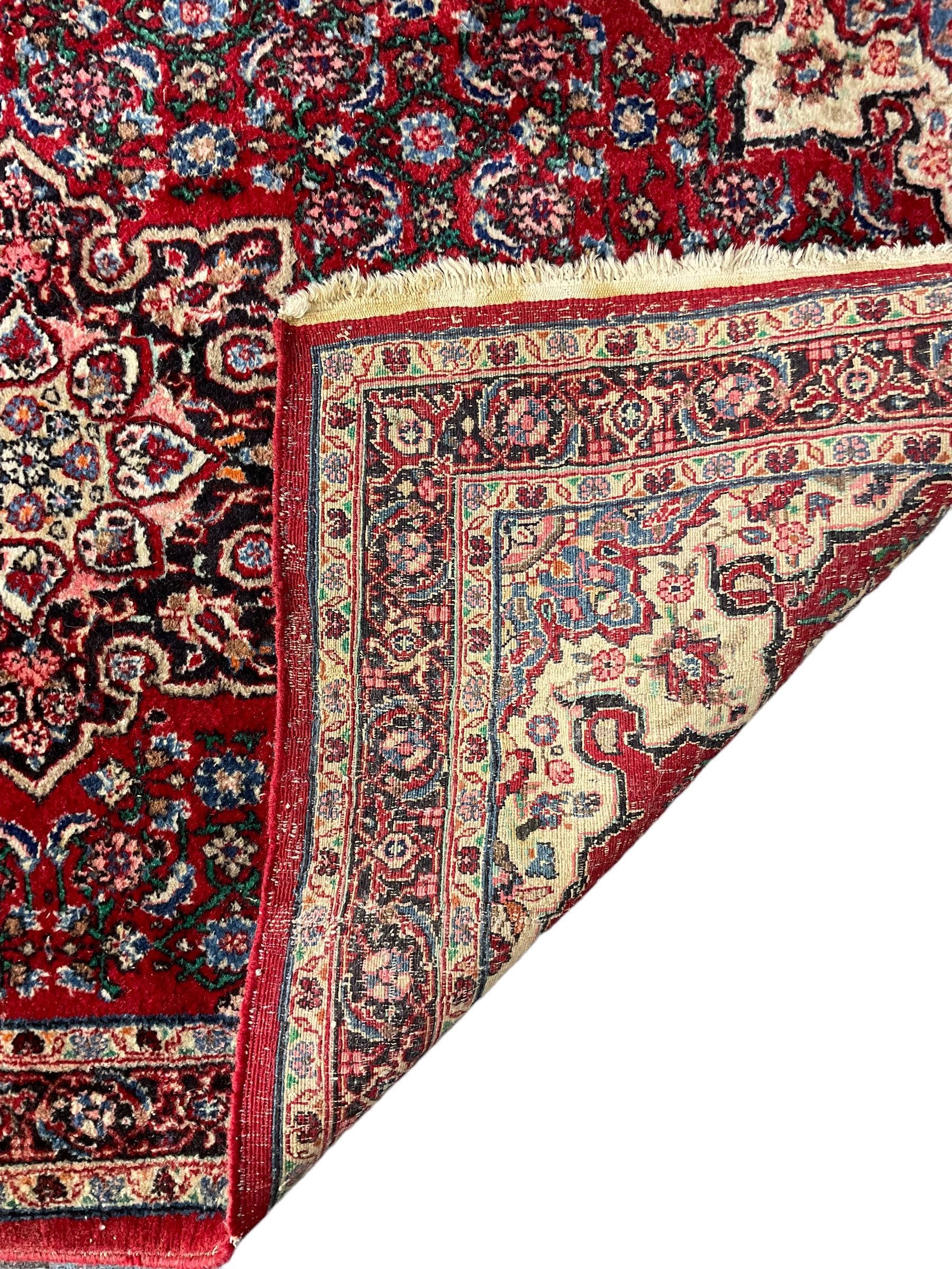 Persian design crimson ground rug, the field decorated with central floral pole medallion and surrounded by foliate patterns with matching spandrels, guarded border with repeating palmette motifs