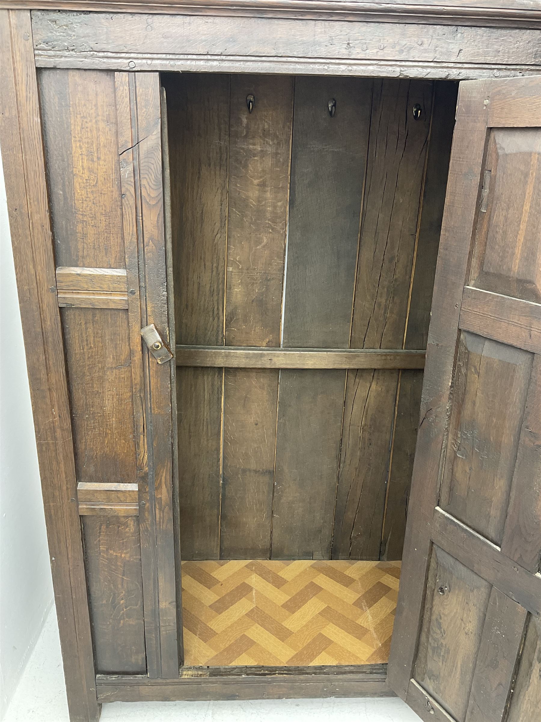 17th century and later oak hall cupboard, panelled front and sides with moulded frame, enclosed by single door with wrought metal hinges and handle, the interior fitted with hooks, on stile supports 