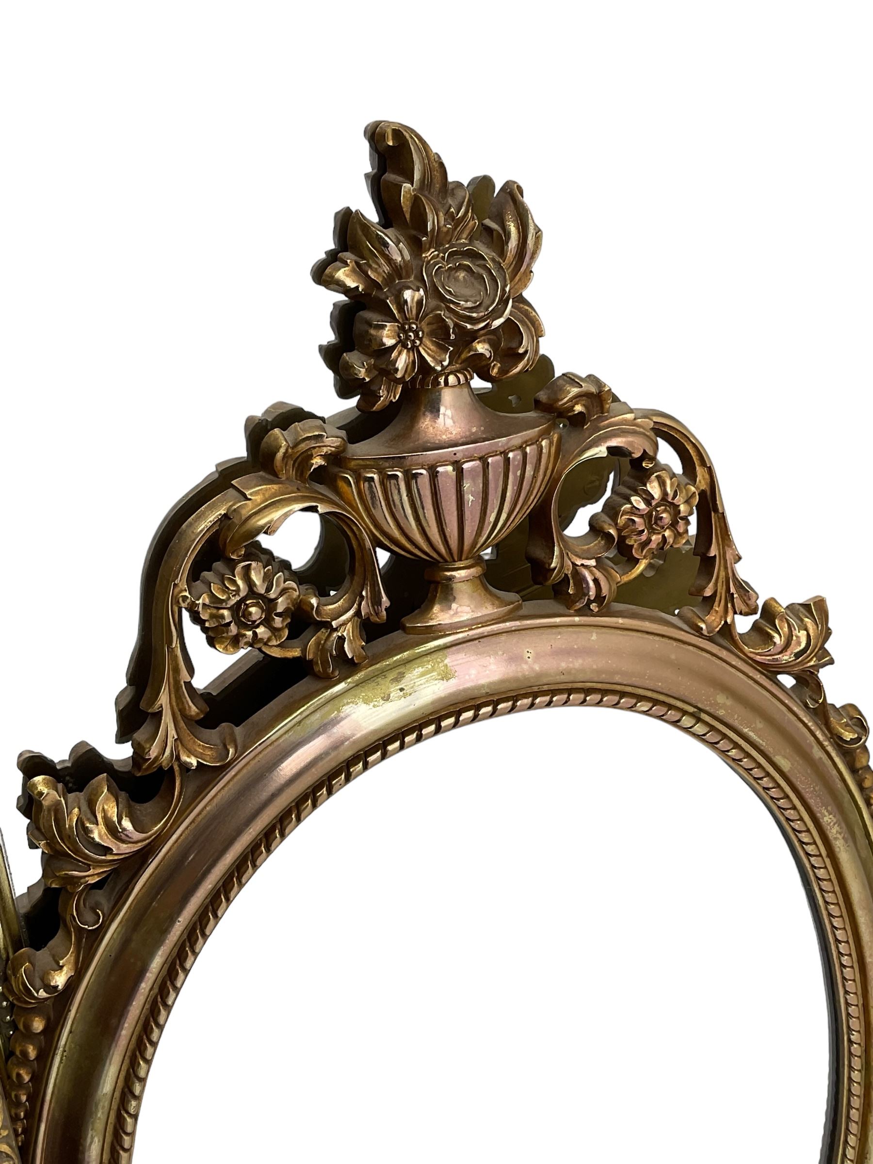 Regency revival style gilt framed oval mirror, the frame with laurel swags topped with urn and flame finial, beaded chain and ram's head motifs, bevelled glass pane; three additional gilt framed mirrors to include one oval and two rectangular (4)