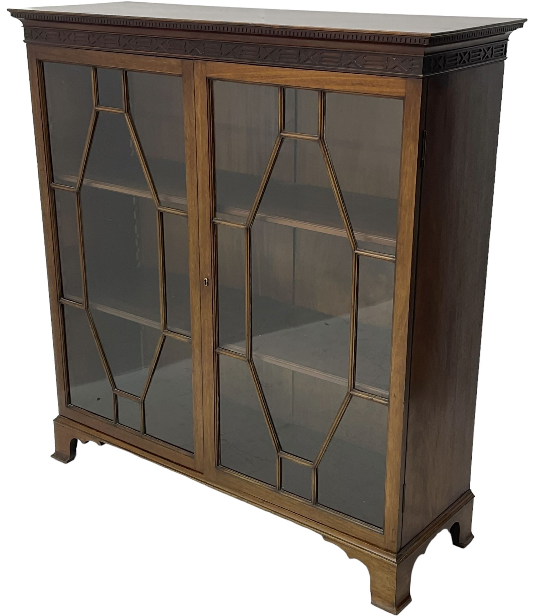 Early 20th century mahogany bookcase, projecting dentil cornice over blind fretwork frieze, enclosed by two astragal glazed doors, on shaped bracket feet 