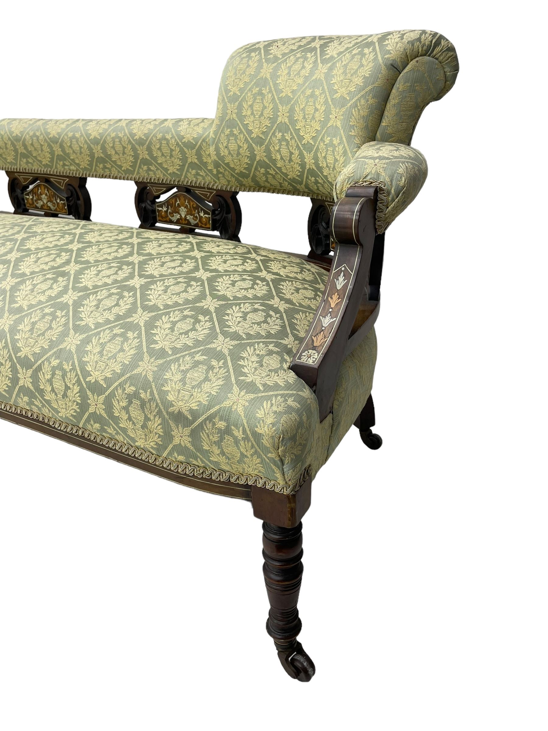 Late Victorian walnut salon settee or chaise lounge, double-ended with rolled back and curved end, upholstered in light aquamarine fabric with raised repeating lozenge pattern, decorated with laurel leaf wreaths and urns, three pierced splats carved with curled leaves, inlaid with dolphins and scrolled foliate motifs in simulated ivory and boxwood, on tapering ring turned supports with brass and ceramic castors (L166, D60, H70cm); together with matching tub-shaped armchair (W61cm, H73cm, D66cm)  