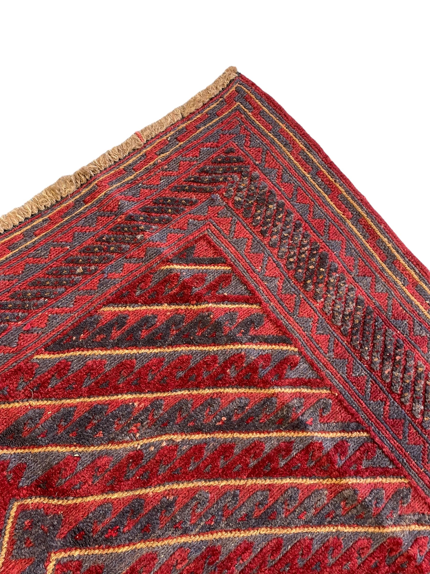 Meshwani indigo and maroon ground rug, the field decorated with a central lozenge with concentric borders containing hook motifs, enclosed by geometric zig-zag guard lines