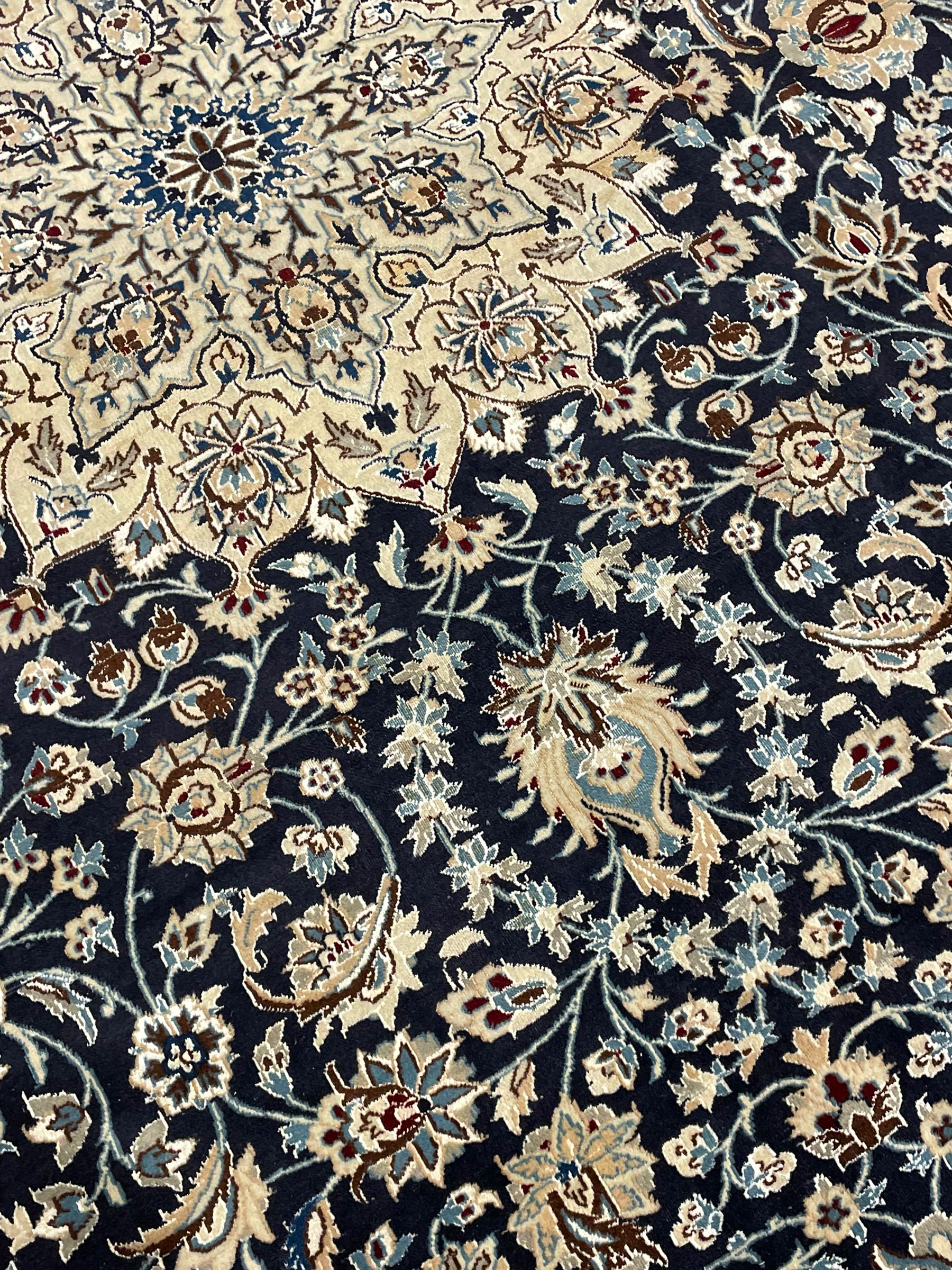 Persian Kashan indigo ground carpet, the central ivory rosette medallion surrounded by trailing and interlaced flower heads and branches, matching spandrels with floral design, the border with scrolling pattern decorated with stylised plant motifs within guards