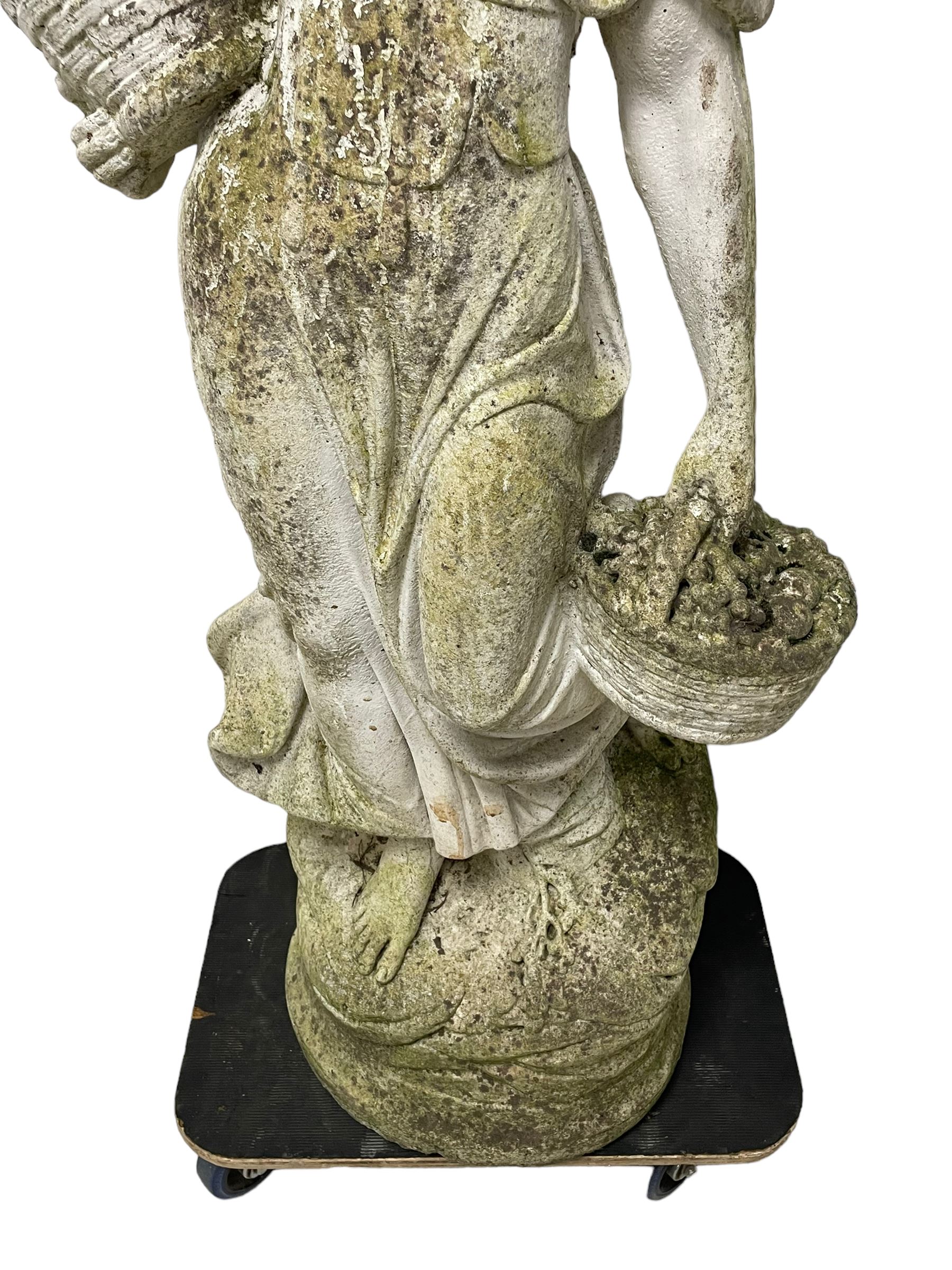 Weathered and painted cast stone garden statue, in the form of an Italian maiden carrying baskets with gathered flora and berries, on a shaped ovoid base