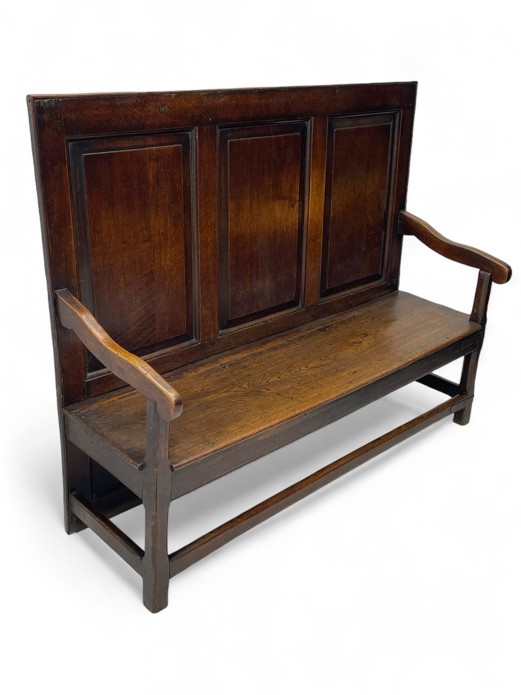 18th century oak settle, the high back with three fielded panels, shaped arms and solid plank seat, standing on square supports joined by stretchers