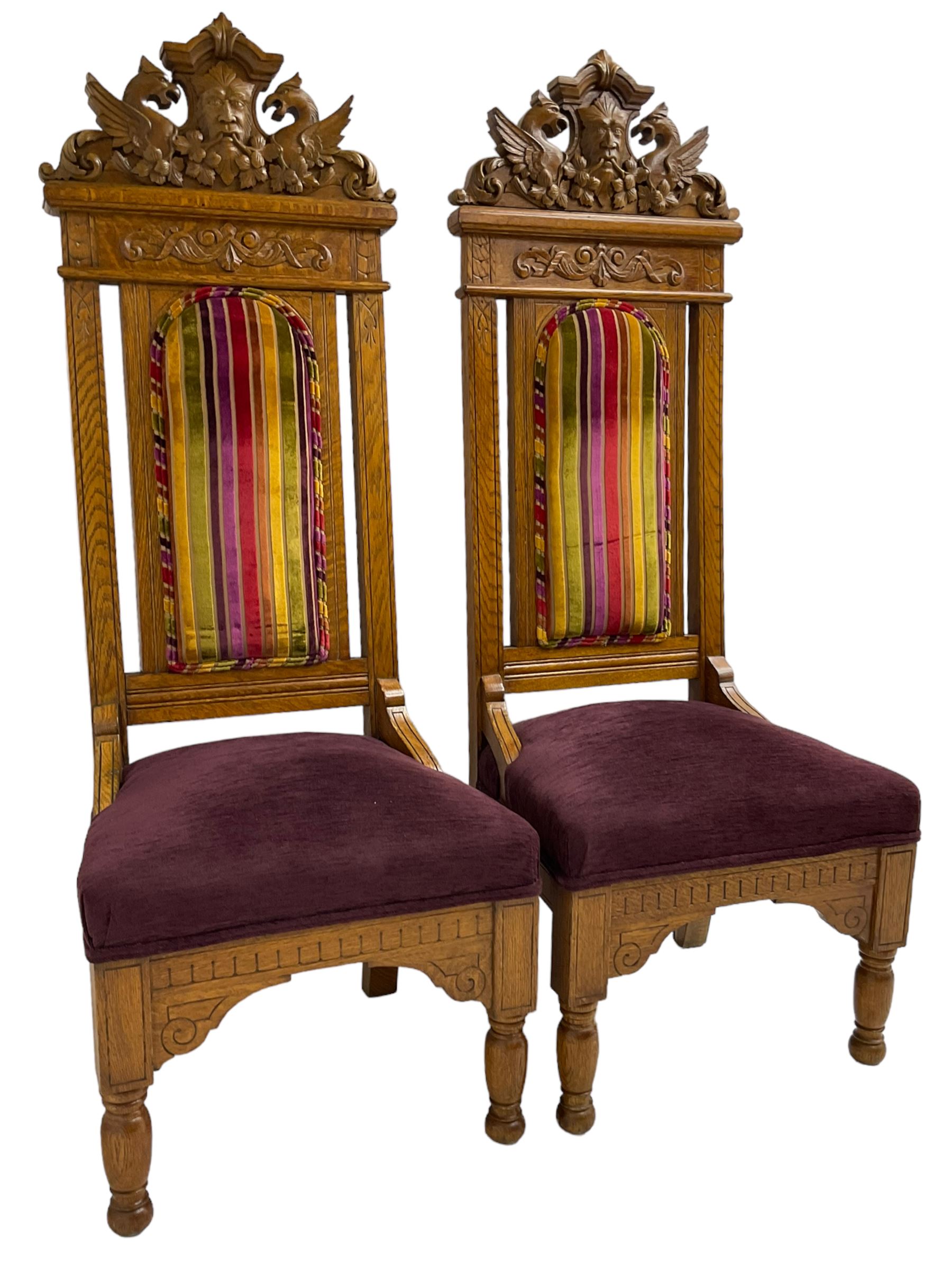 Set of six 20th century Carolean design oak high back chairs, the pediment carved with dragons and central Green Man mask with trailing foliage, the backs upholstered in striped fabric, on turned front supports