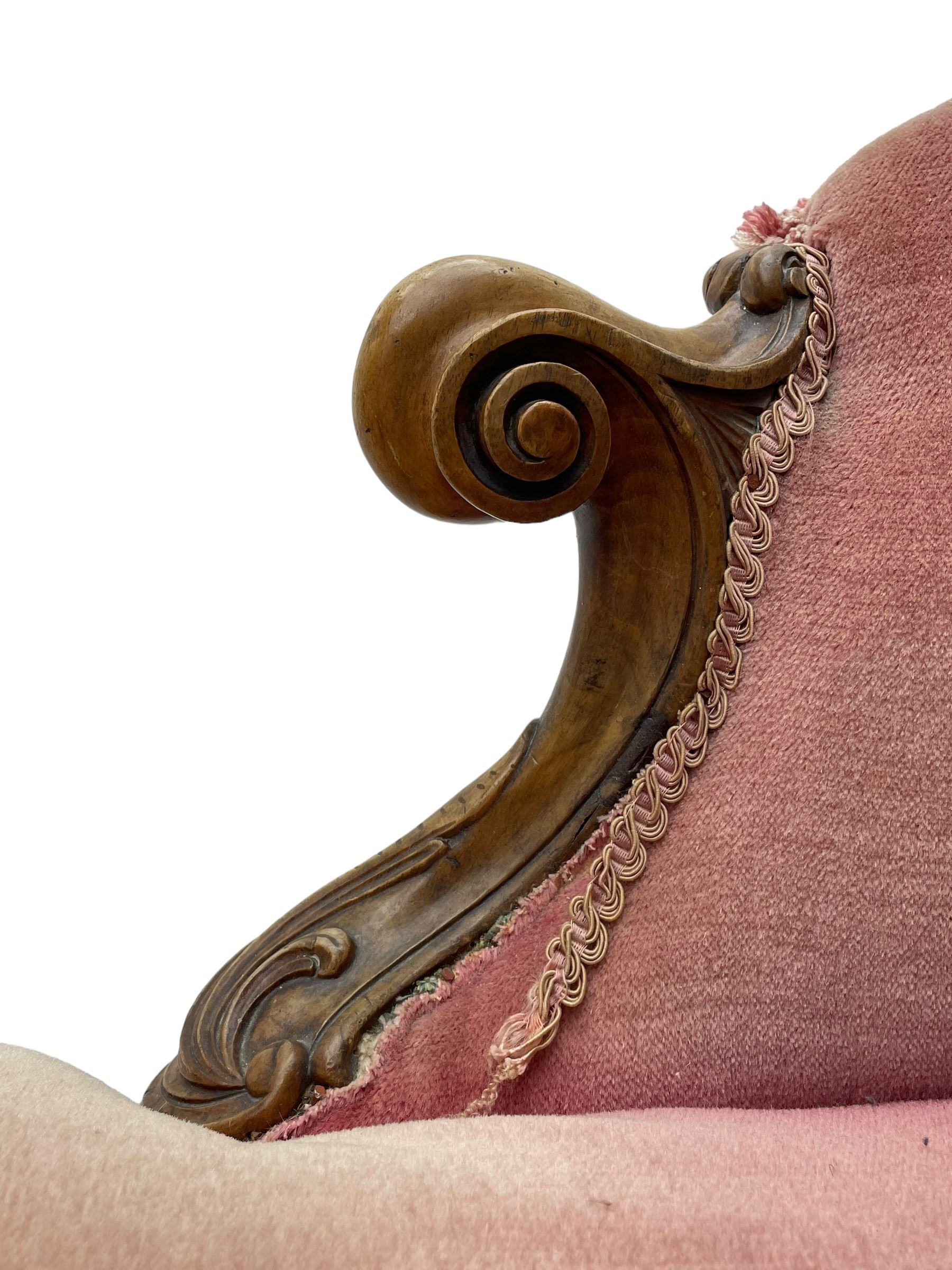 Victorian walnut framed tete-a-tete loveseat, scrolled arm terminals with moulded foliate decoration, buttoned backs and sprung seat upholstered in pale pink velvet, raised on cabriole supports with applied flower heads and scroll feet terminating to ceramic castors