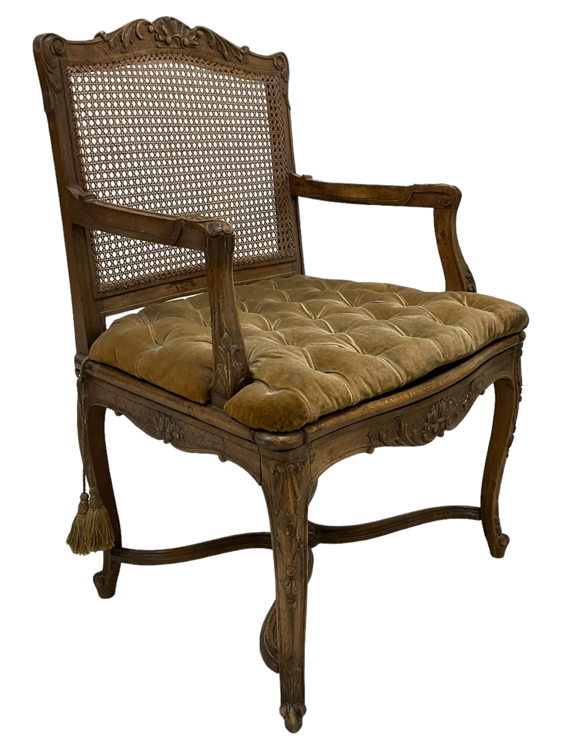 Late 19th century French carved beech open elbow chair, shaped cresting rail carved with central shell and curl leafage, cane work seat and back with buttoned loose seat cushion, the open arms carved with scrolled terminals and acanthus leaves, on cabriole supports with carved decorated united by shaped and moulded x-framed stretchers 