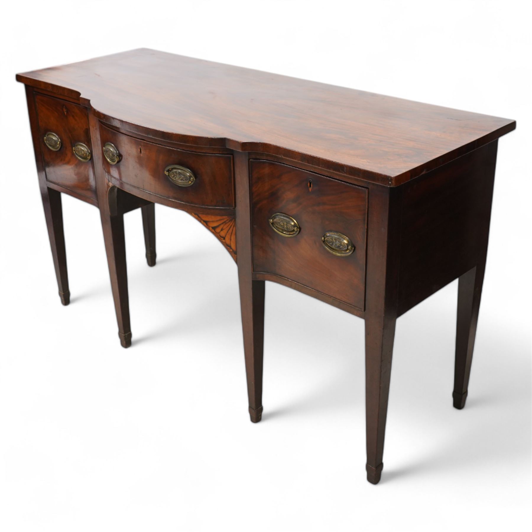 George III mahogany break bow-front sideboard, fitted with three drawers, the corner brackets inlaid with quarter shell motifs, pressed brass oval handle plates decorated with oak leaves and acorns, on square tapering supports