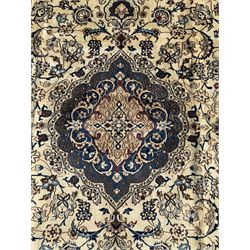 Persian Nain ivory ground carpet, central indigo medallion, the busy floral field decorated with scrolling vines and flower heads in shades of blue, beige, and red, wide guarded border with repeating palmettes and foliate motifs