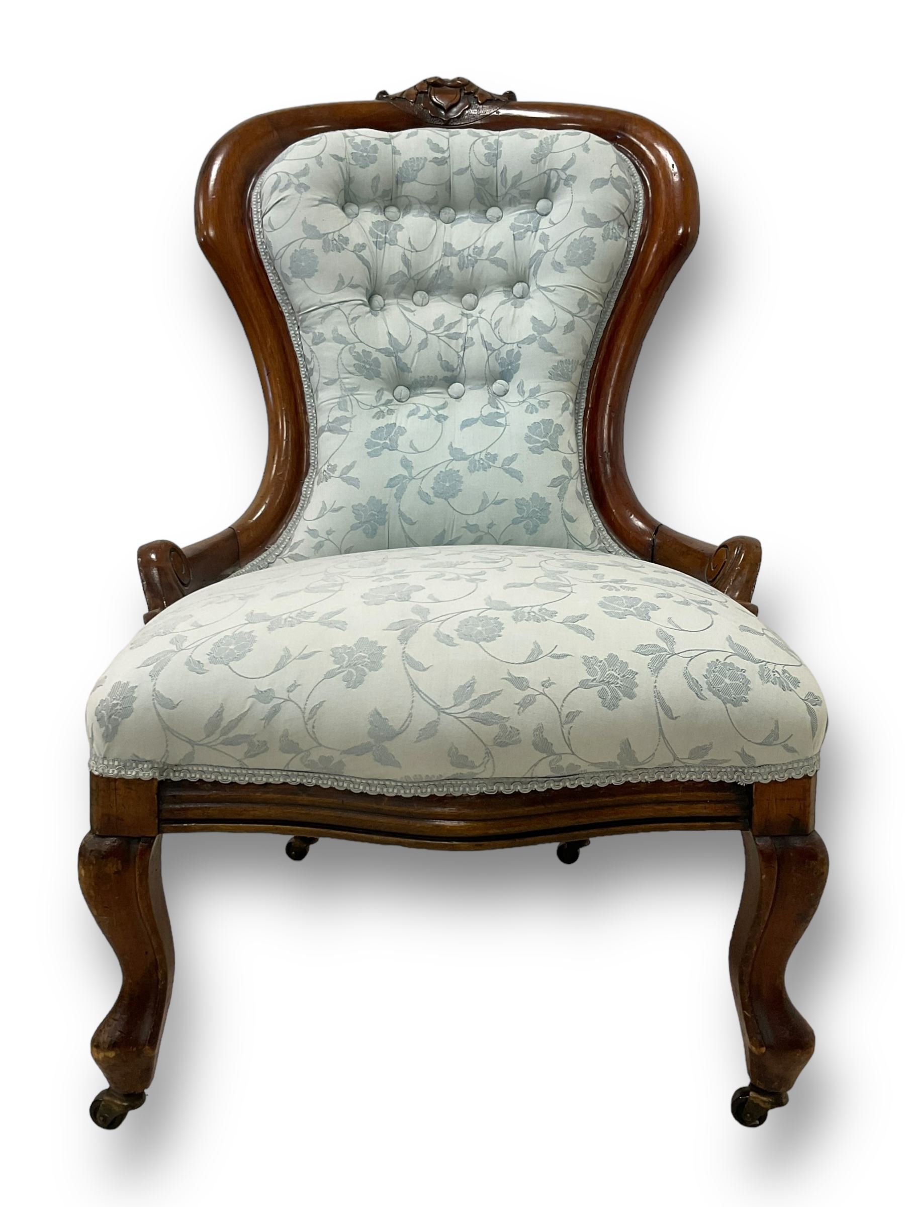 Victorian walnut nursing chair, the curved cresting rail carved with central cartouche and scroll leaves, upholstered in pale blue fabric decorated with trailing floral design, on cabriole front feet 