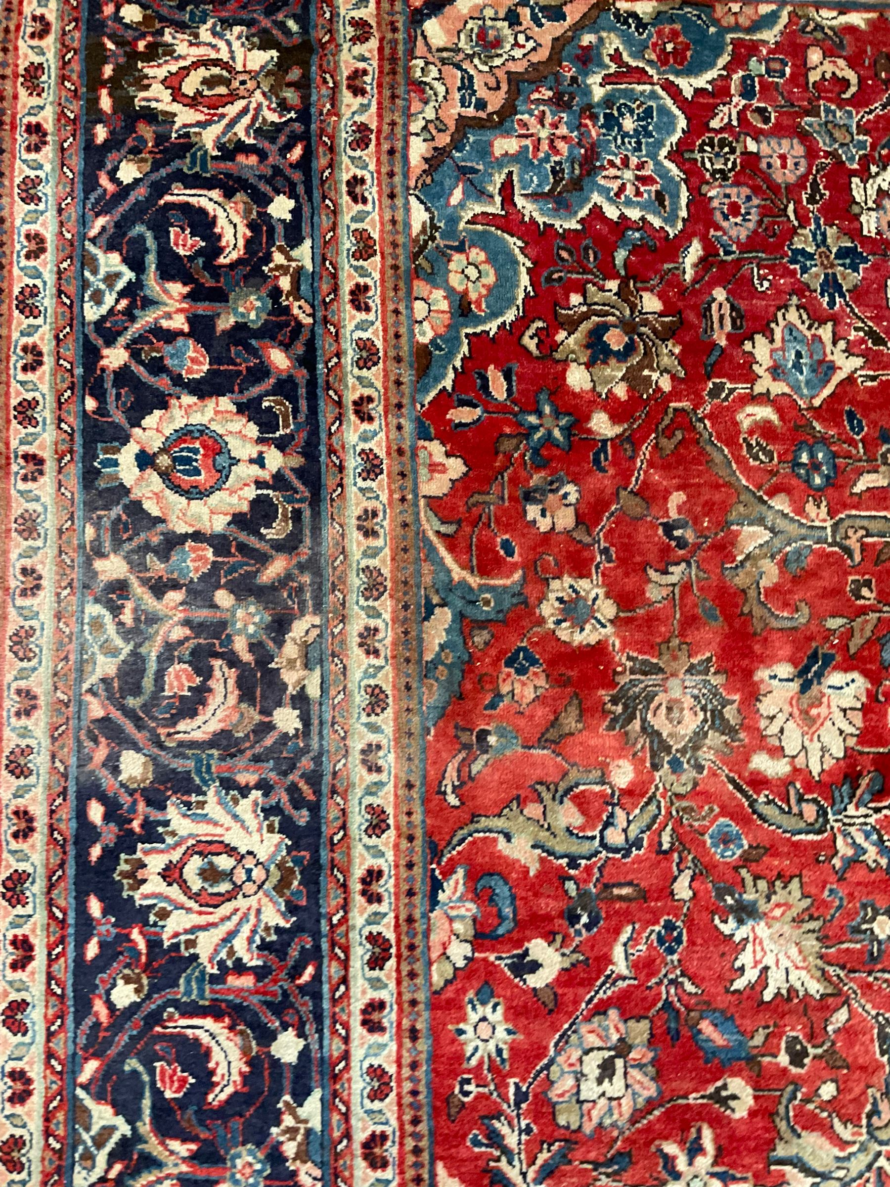 Persian Kashan crimson ground carpet, central shaped pale ground medallion surrounded by interlacing branches and stylised floral motifs, indigo main border with scrolling foliage design, within guard stripes 