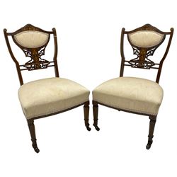 Pair of Edwardian inlaid rosewood bedroom chairs, the shaped cresting rail inlaid with extending floral decoration, upholstered back over pierced and scroll carved splat decorated with further floral inlays, upholstered sprung seats, on square front supports with shaped peg feet