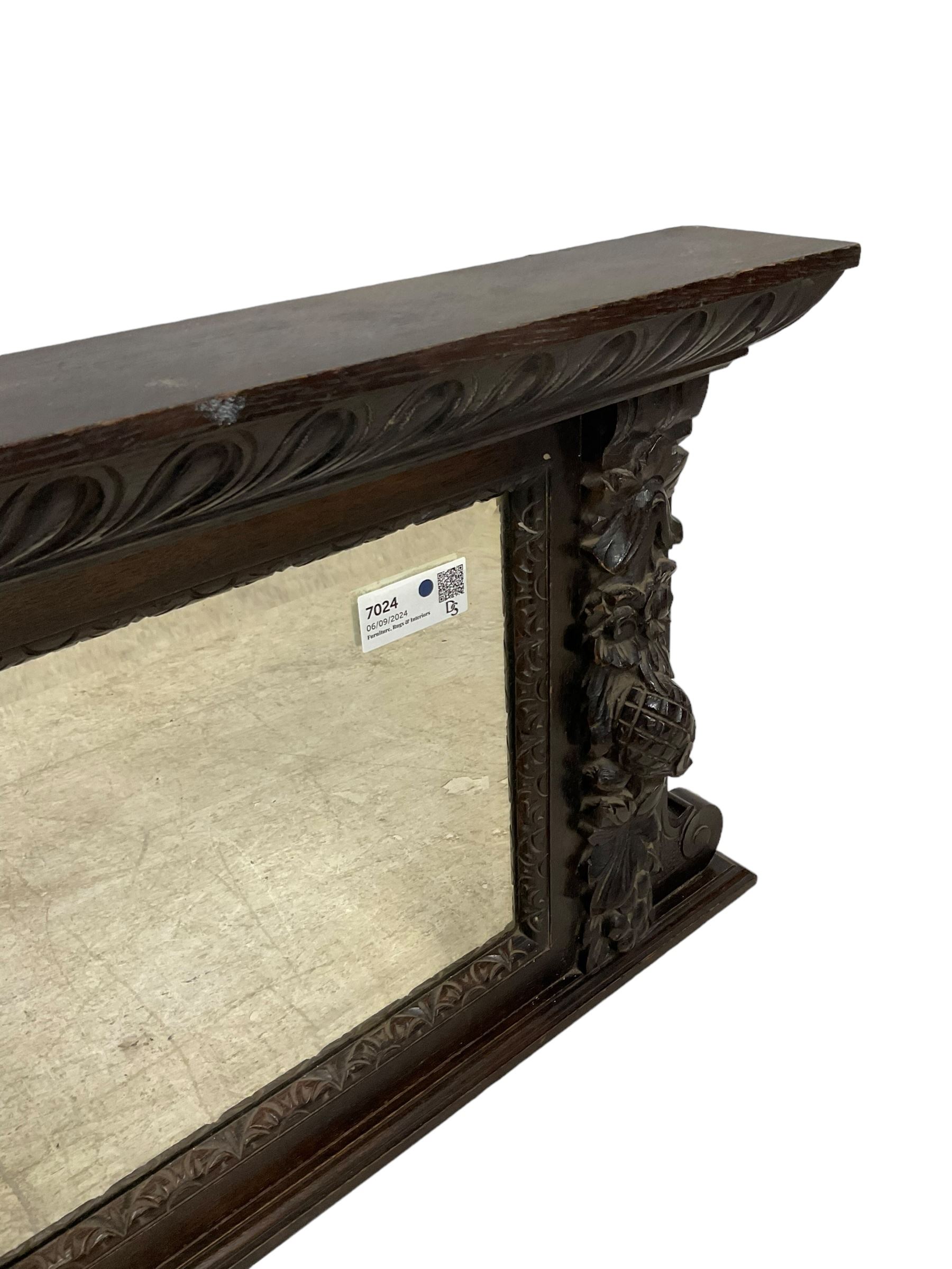 Victorian heavily carved oak wall mirror, projecting gadroon carved ovolo cornice, bevelled mirror plate within a lunette carved frame, decorated with applied fruit and foliage carved mounts, scroll carved brackets 