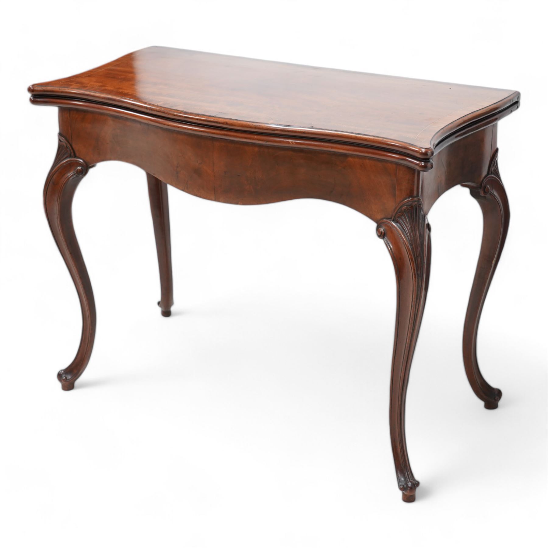 George III inlaid mahogany card table of serpentine form, the shaped rectangular fold-over top decorated with cross-banding and chequered inlay, opening to reveal a baize lined interior, the shaped apron over moulded cabriole supports with scroll and scallop carved knees, on scroll feet