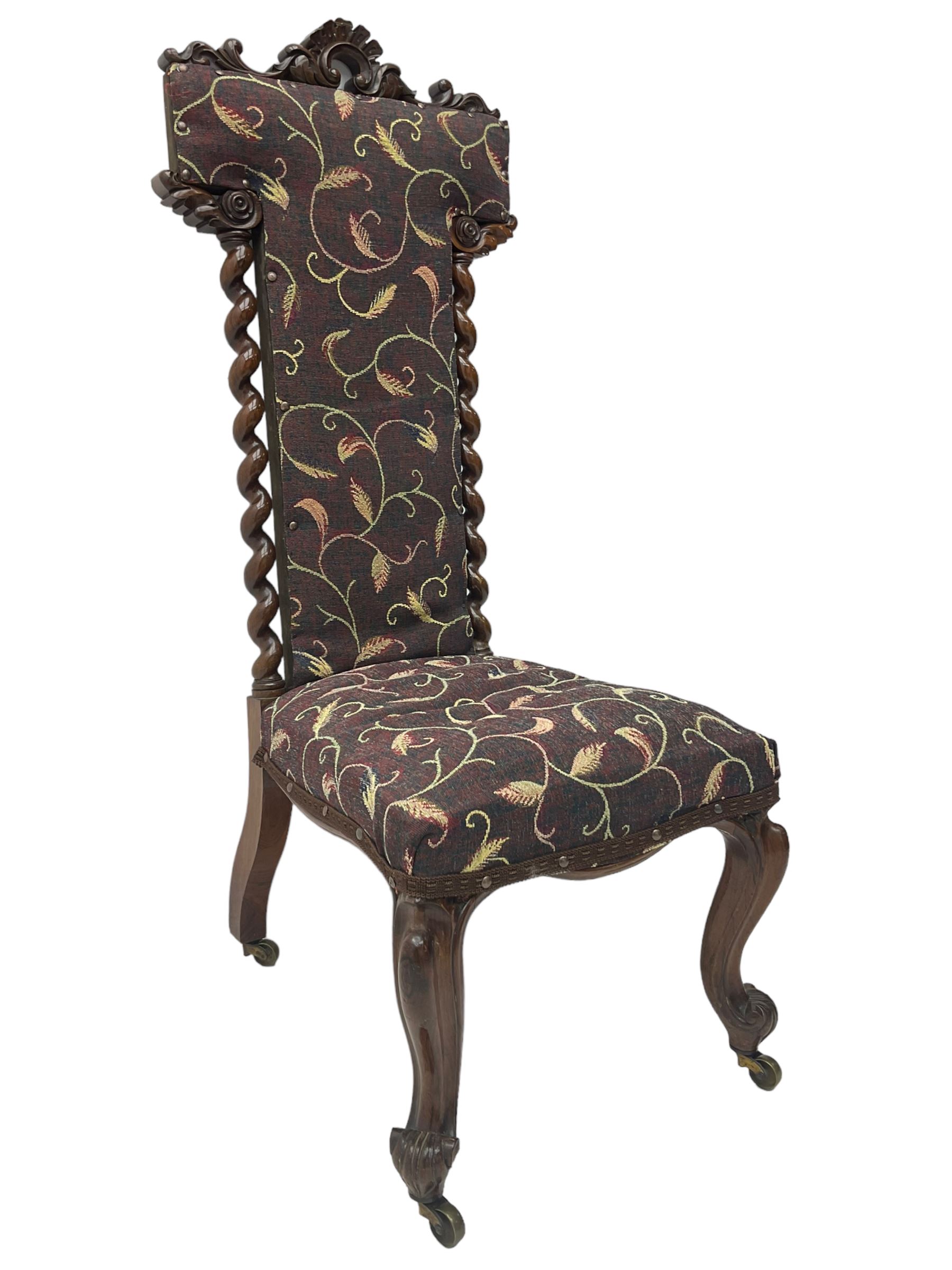 Victorian walnut prie-dieu chair, cresting rail carved with cartouche and extending scrolling foliage, back flanked by spiral turned column uprights, upholstered in foliate patterned fabric, raised on cabriole supports with scroll feet and castors