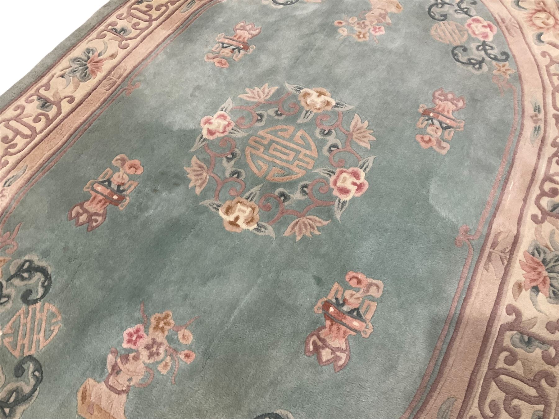 Chinese pale turquoise ground washed woolen rug, oval form decorated with bouquets of floral designs and Chinese characters, enclosed by a wide guard band