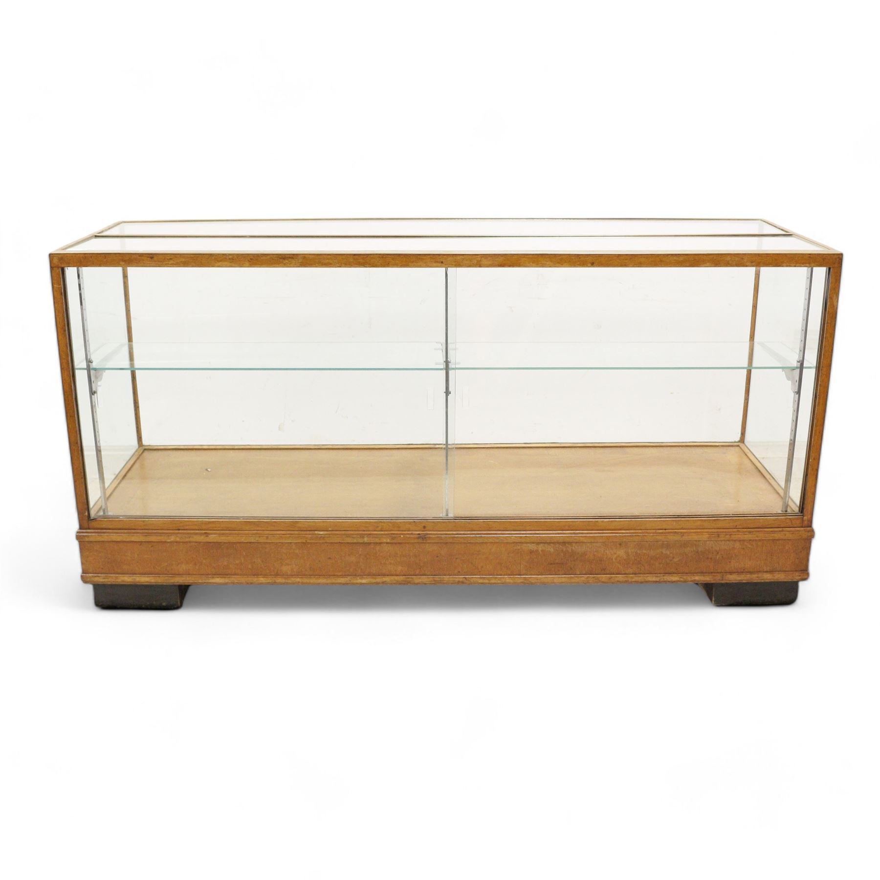 Early 20th century glazed oak and brass bound shop's display cabinet or haberdashery cabinet, fitted with two sliding glass doors, two glass shelves on chromed metal supports, black finish block feet