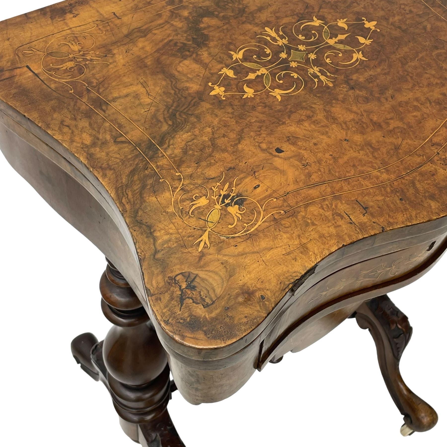 Victorian inlaid figured walnut games table, the serpentine fold-over top inlaid with scrolling foliate decoration, the top opens to reveal cribbage, backgammon and chess boards, single drawer over sliding storage well, on twin pillar supports united by double turned stretchers, on foliage carved out-splayed supports with brass and ceramic castors 