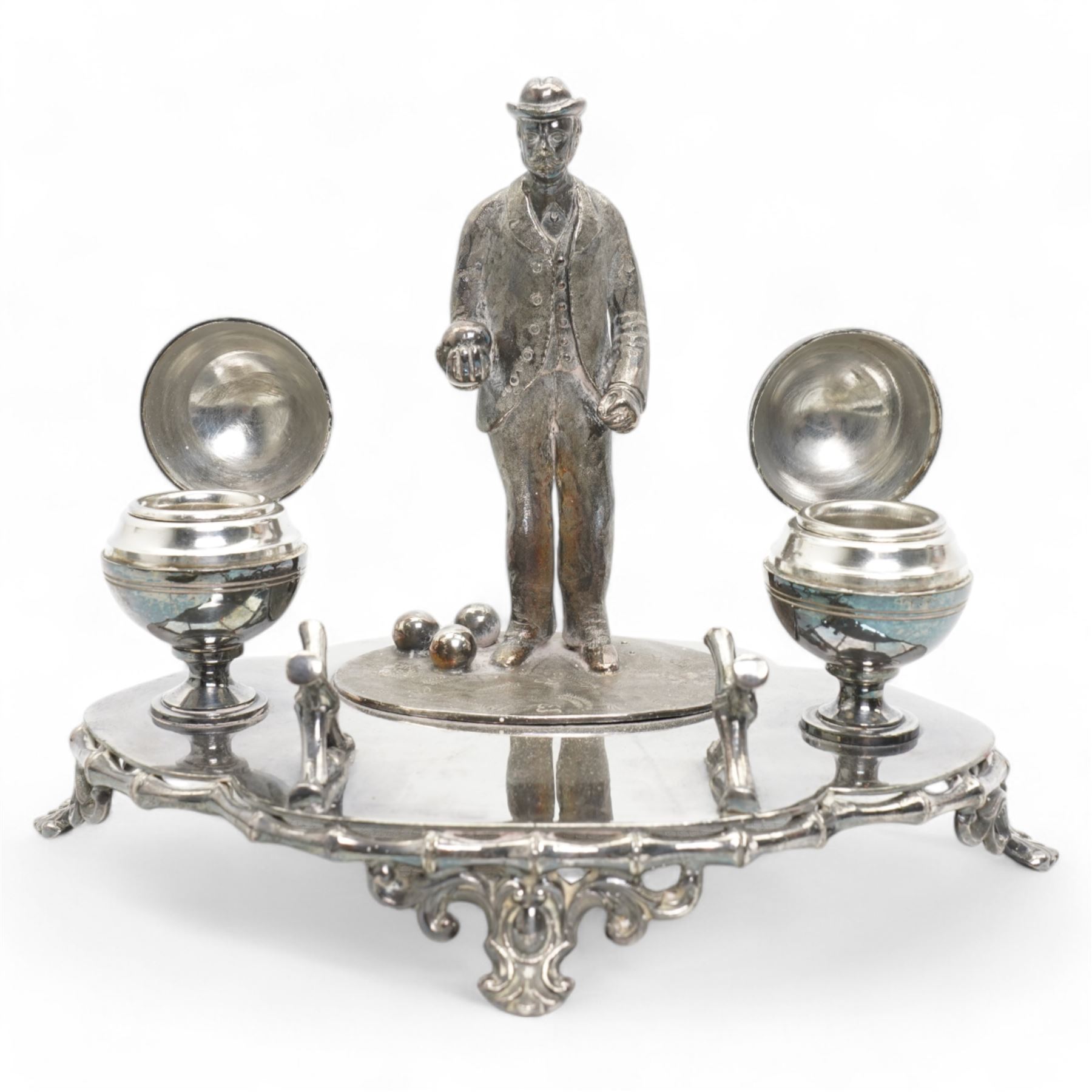 Victorian silver-plated inkstand by James Dixon & Sons, the quatrefoil base surmounted with a figure of a lawn bowler stood upon an oval grass base, with three lawn bowls by his feet, the inkwells formed as two bowls, each with hinged covers and silver-plated liners, bamboo moulded pen rest and gallery, supported by four pierced and splayed feet, L22cm x H17cm