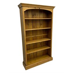 Pine open bookcase, projecting moulded cornice over arched frieze, fitted with four adjustable shelves, on plinth base