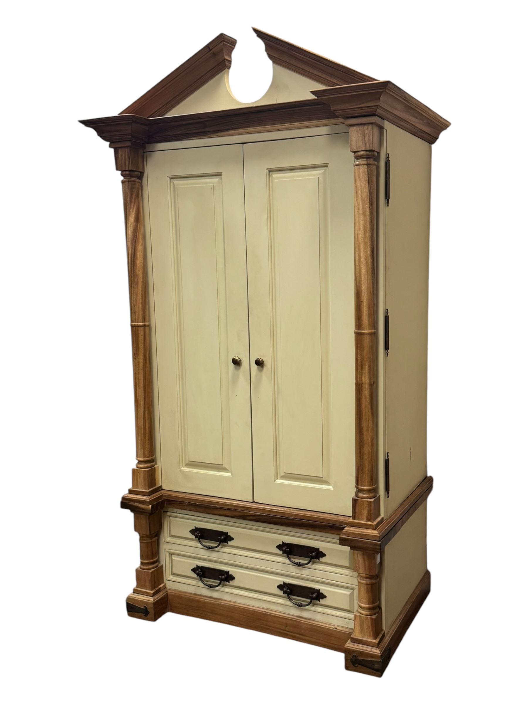 Hardwood and cream painted kitchen larder cupboard, sloped pediment over two panelled doors, the interior fitted with slides, drawers and storage shelves, two long drawers below, mounted by turned pilasters, on metal bound moulded plinth base