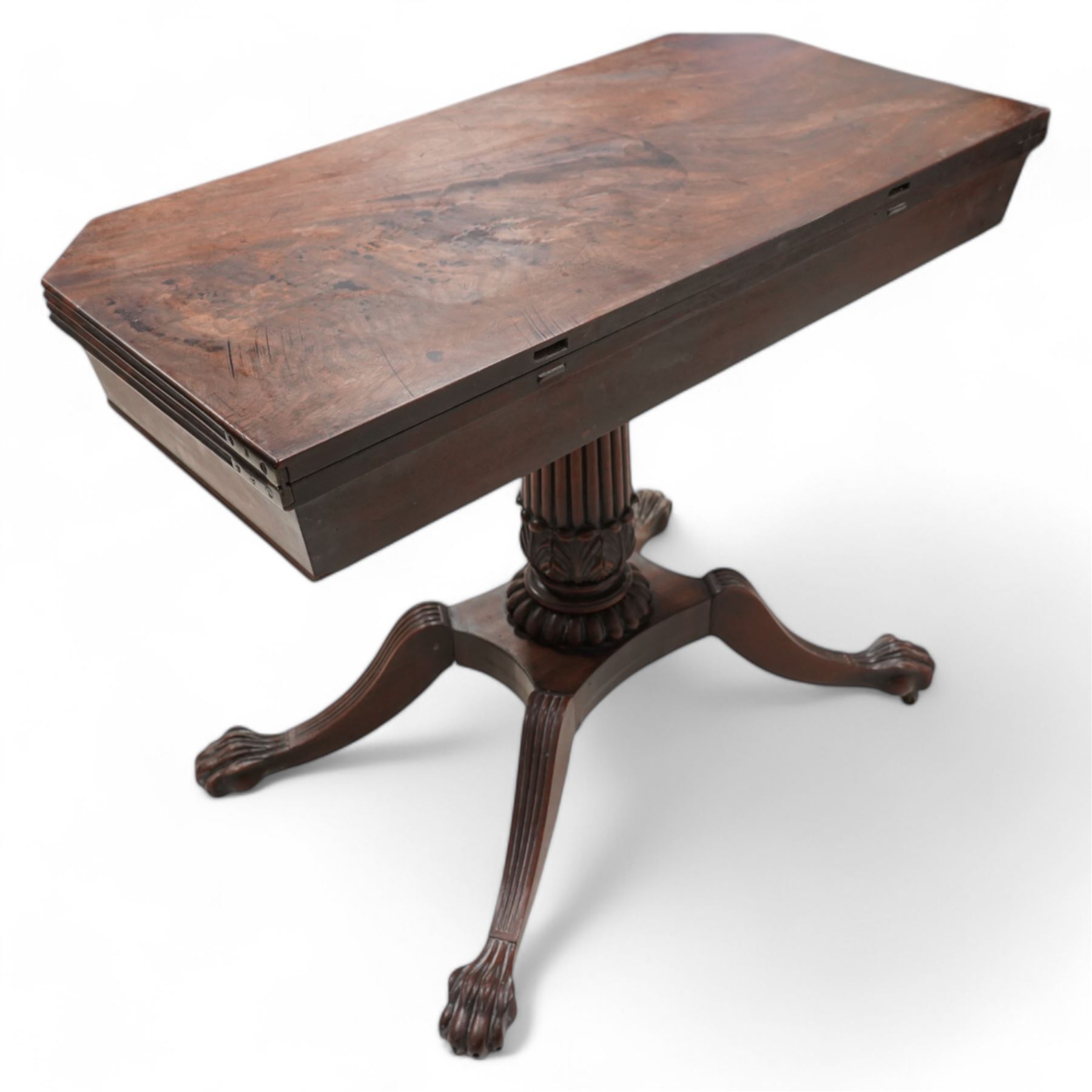 Regency mahogany card table, rectangular swivel and fold-over top with canted corners and reed-moulded edge, raised on a reeded pedestal with acanthus carved terminal and gardrooned collar, the concave rectangular base terminating to splayed supports with large paw feet on castors