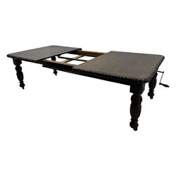 19th century heavily carved oak extending dining table, rectangular top with rounded corners and carved gadrooned edge, extending via winding mechanism with two additional leaves, raised on acanthus leaf-carved baluster supports terminating in ceramic castors