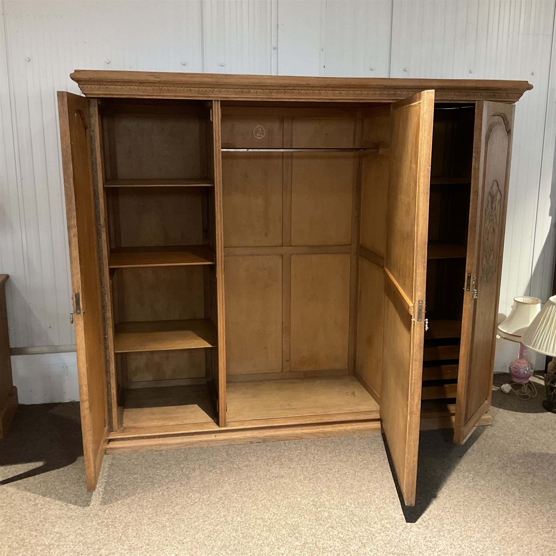 Late 19th century oak triple wardrobe, wide central bevelled mirror door, flanked by two panelled doors each carved with scrolling leaves and flower heads, on moulded skirt base 