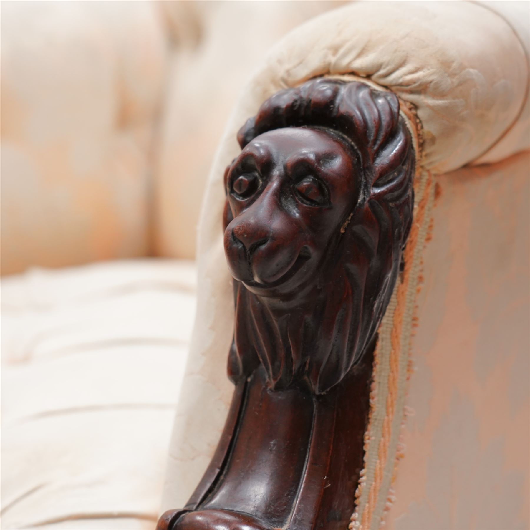 Victorian mahogany framed armchair, moulded and rolled uprights, upholstered in buttoned cream foliate pattern fabric, carved lion mask arm terminals, on turned and globular carved front feet, brass castors 