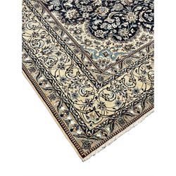 Persian Kashan indigo ground carpet, the central ivory rosette medallion surrounded by trailing and interlaced flower heads and branches, matching spandrels with floral design, the border with scrolling pattern decorated with stylised plant motifs within guards