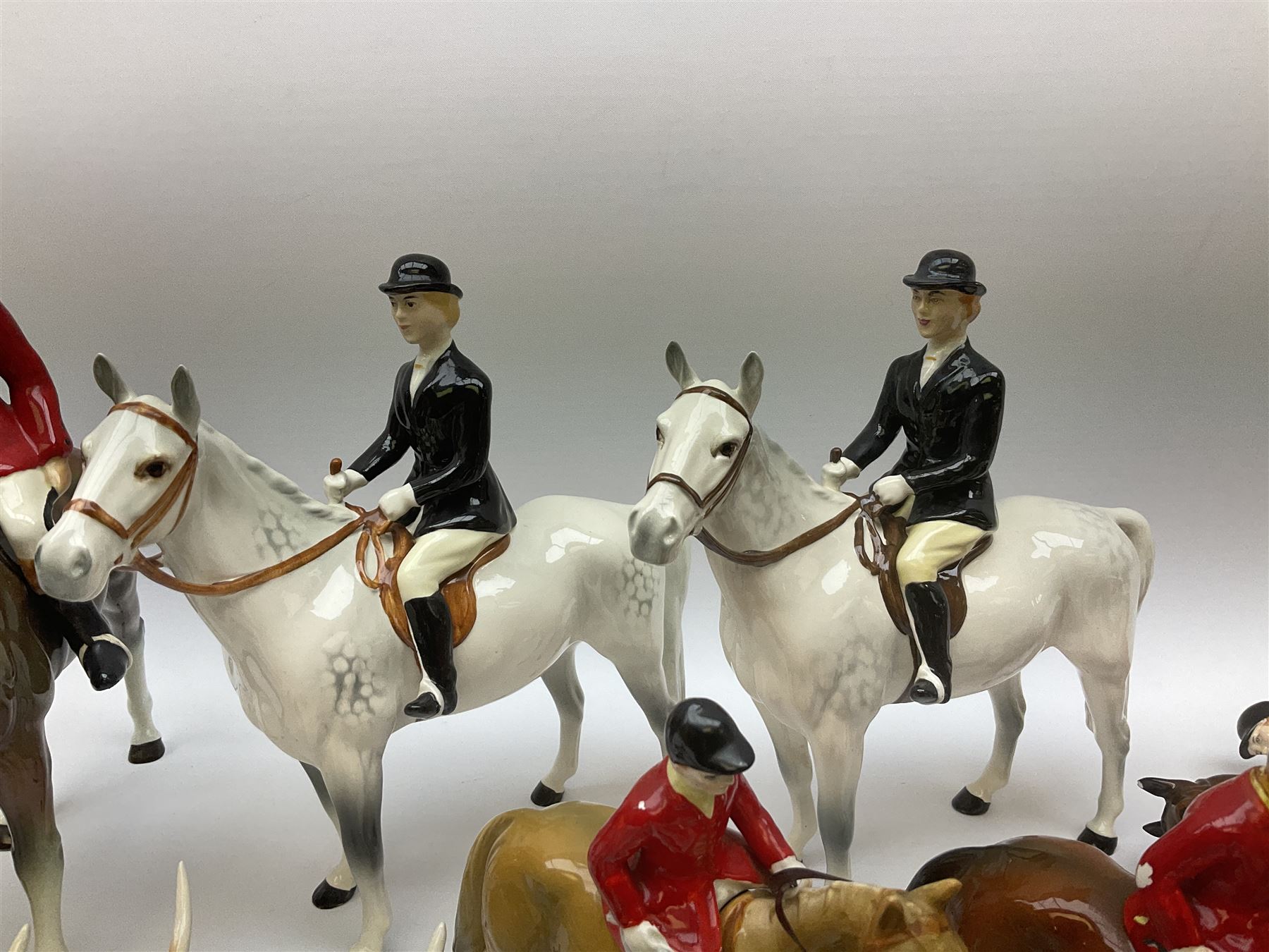 Beswick Hunting Group, comprising: two huntswoman on grey horses, model no 1730, huntsman on a bay horse, model no 1501, a seated fox, model no 1748, eighteen fox hounds and a spaniel, model no 967, all with printed marks beneath, together with three other ceramic huntsman on horseback and two hounds. 