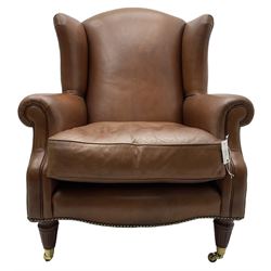 Georgian design wingback armchair, upholstered in brown leather with stud band and piping, turned and fluted front feet on brass cups and castors