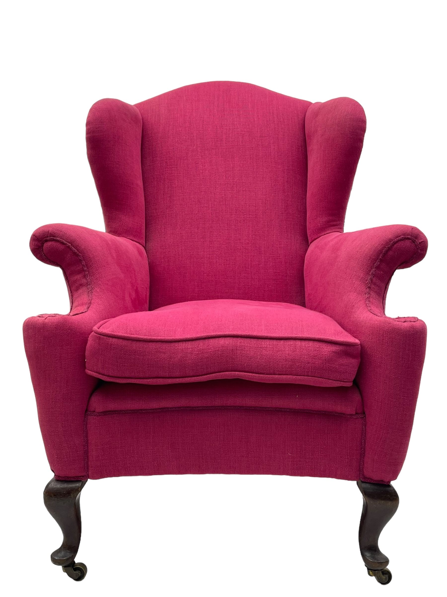 Georgian design hardwood-framed wingback armchair, arched cresting rail over curved wingback, rolled arms on scrolled cushioned supports, reverse bow-front, upholstered in claret red fabric with loose seat cushion, on cabriole front feet and brass castors 