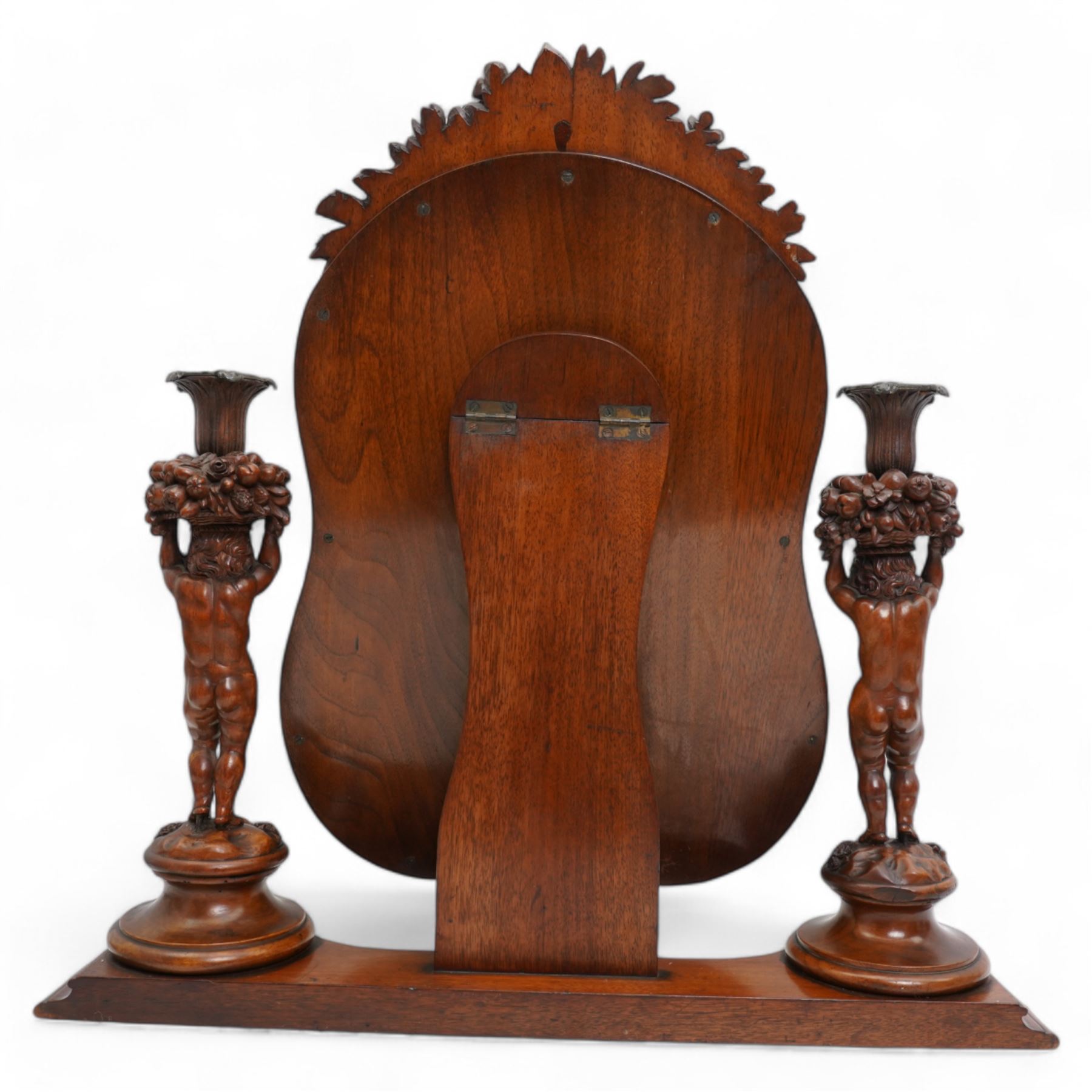 Late 19th century Northern European carved walnut dressing table mirror, the moulded arch top frame carved with flower heads and foliage, flanked by two putto holding baskets of flowers and fruit with candle sconces, on shaped moulded base, plain mirror plate 