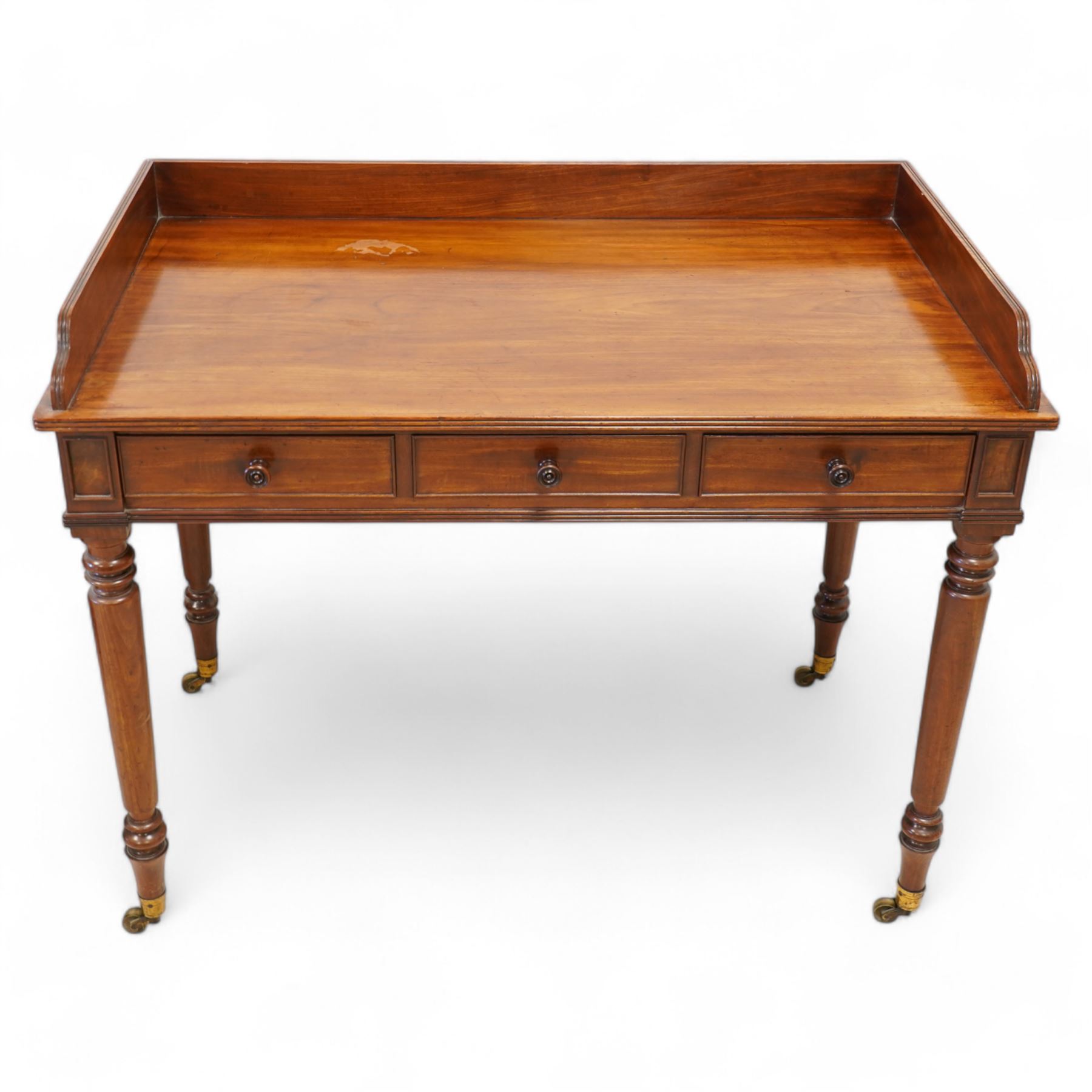 Gillows, Lancaster - early 19th century mahogany writing table, reeded three-quarter gallery over rectangular top with reed moulded edge, fitted with three cocked-beaded drawers with turned handles, the central drawer stamped 'Gillows Lancaster'. on turned supports with brass cups and castors 