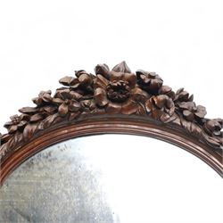 Late 19th century Northern European carved walnut dressing table mirror, the moulded arch top frame carved with flower heads and foliage, flanked by two putto holding baskets of flowers and fruit with candle sconces, on shaped moulded base, plain mirror plate 