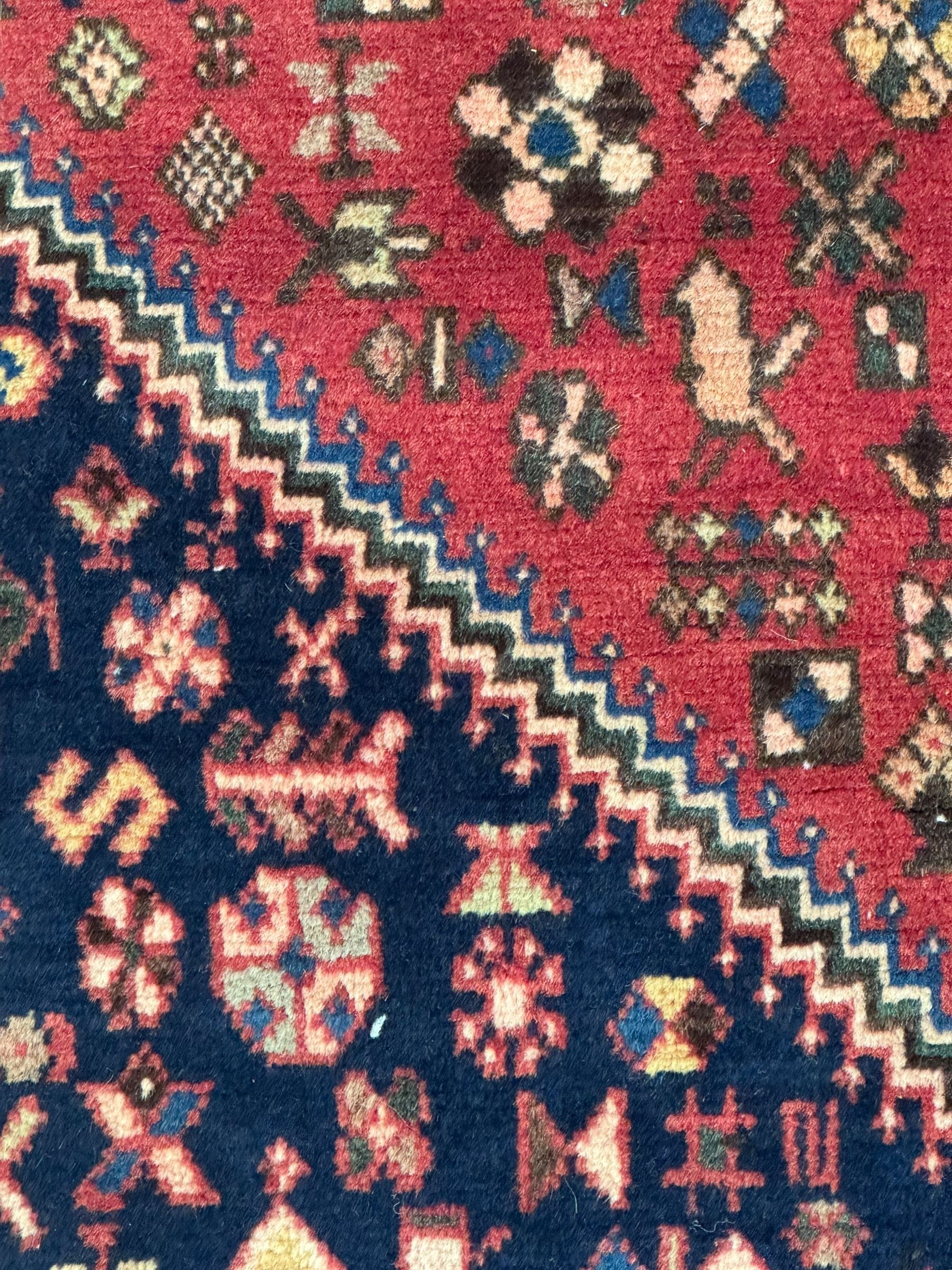 South West Persian Abadeh crimson ground rug, indigo ground with crimson lozenge field, decorated all over with small stylised motifs of flowerheads, hooks, animals and birds, guarded border decorated with trailing leaves and stylised plant motifs 