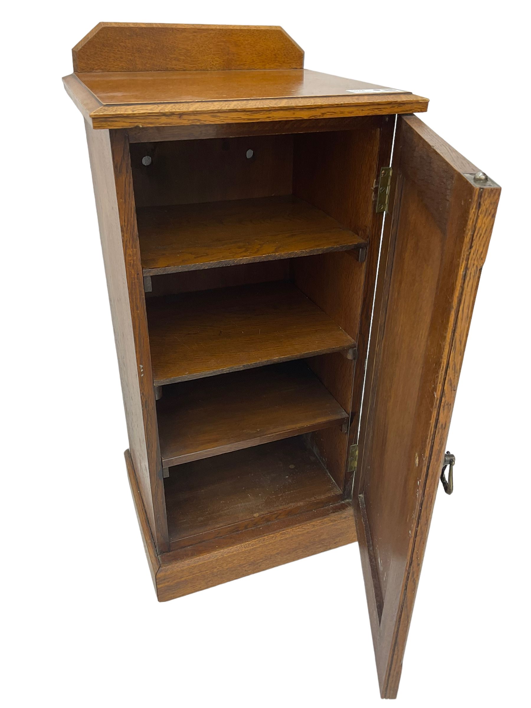 Edwardian oak bedside cabinet, raised back over moulded top, enclosed by panelled door, the interior fitted with shelves, on chamfered plinth base 