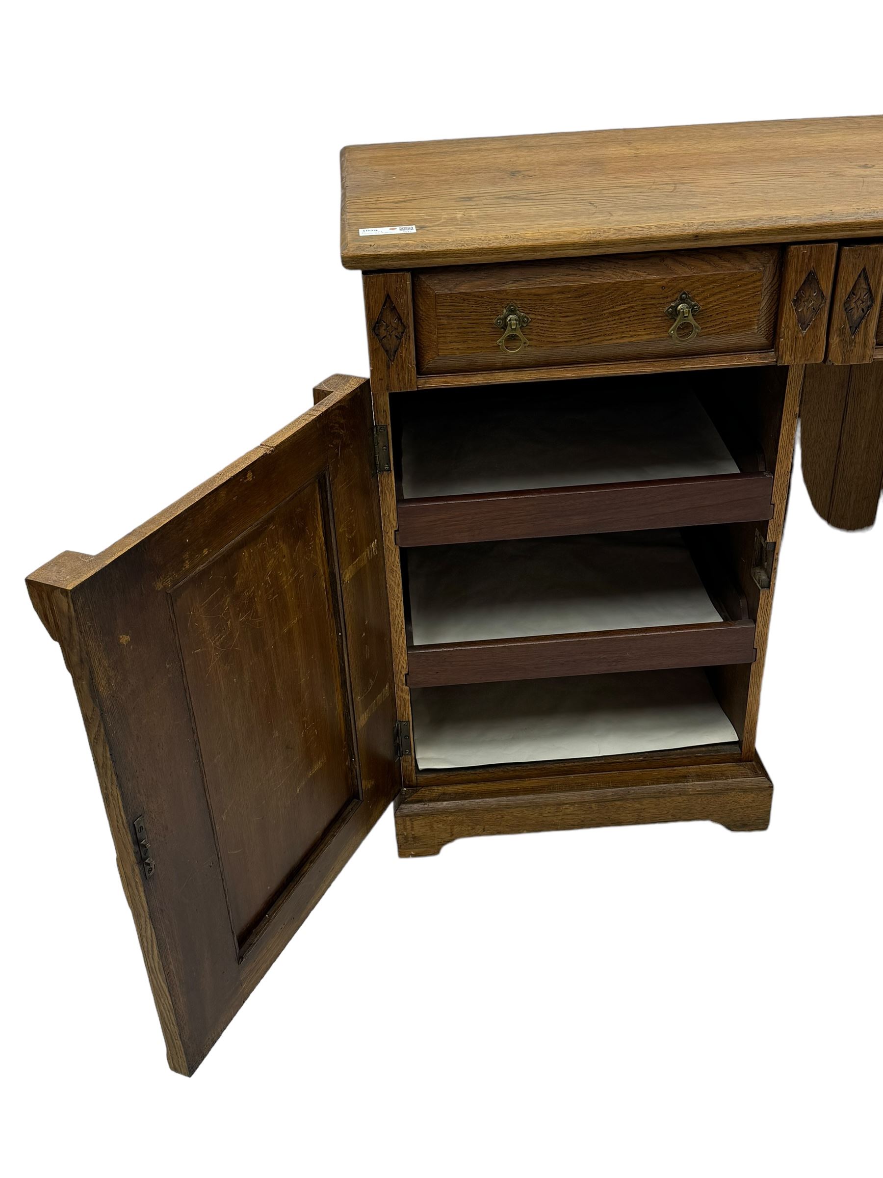 Late Victorian oak twin pedestal desk, chamfered rectangular top over three convex front edge drawers and two panelled cupboards, flanked by carved supports with roundels and diamond motif, on bracketed plinth base