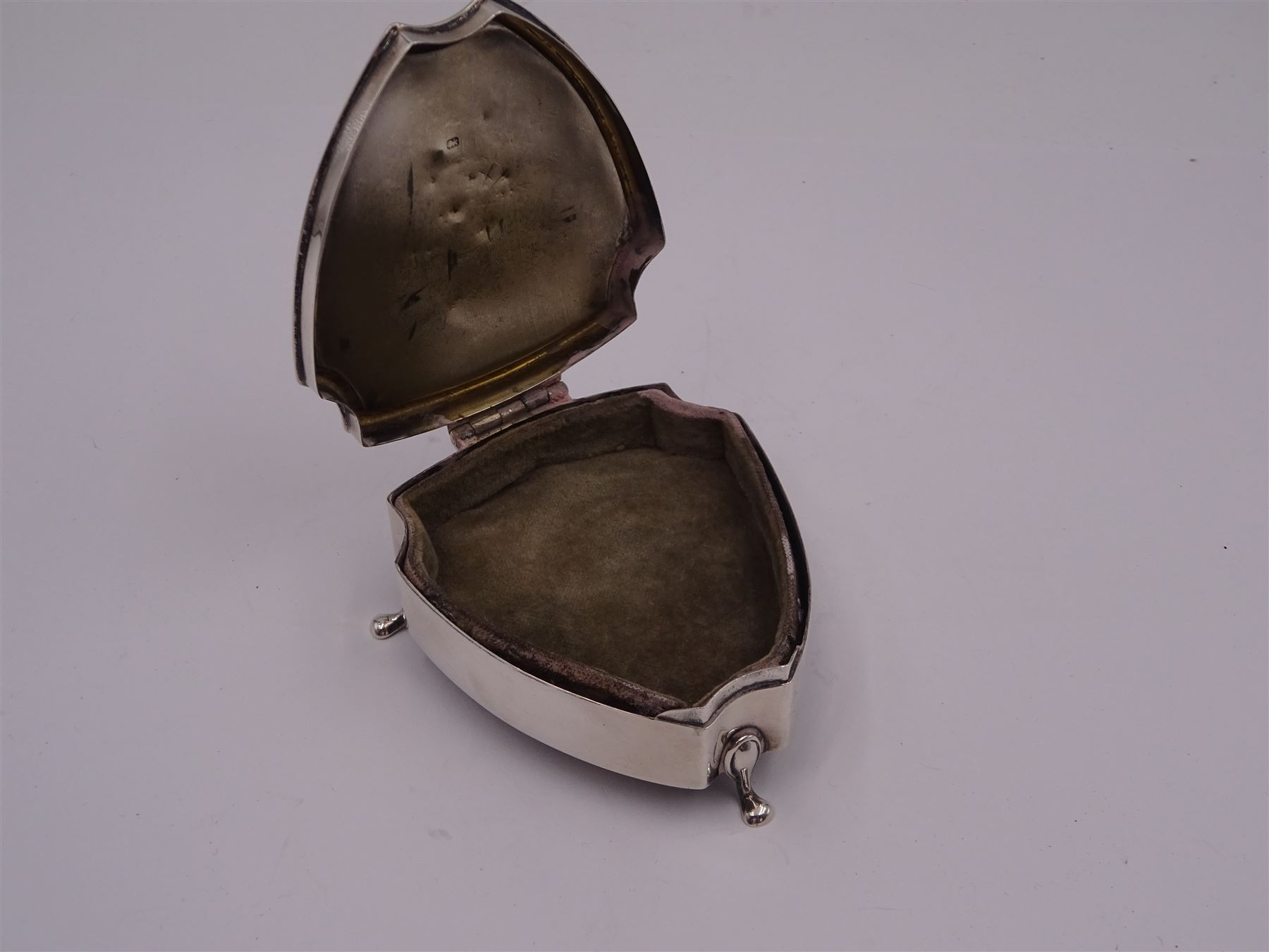 Early 20th century silver mounted trinket box, of shield form, with engine turned decoration and engraved circular cartouche to hinged cover, opening to reveal green velvet interior, upon three pad feet, hallmarked Walker & Hall, Sheffield 1914, H3.5cm, W7cm